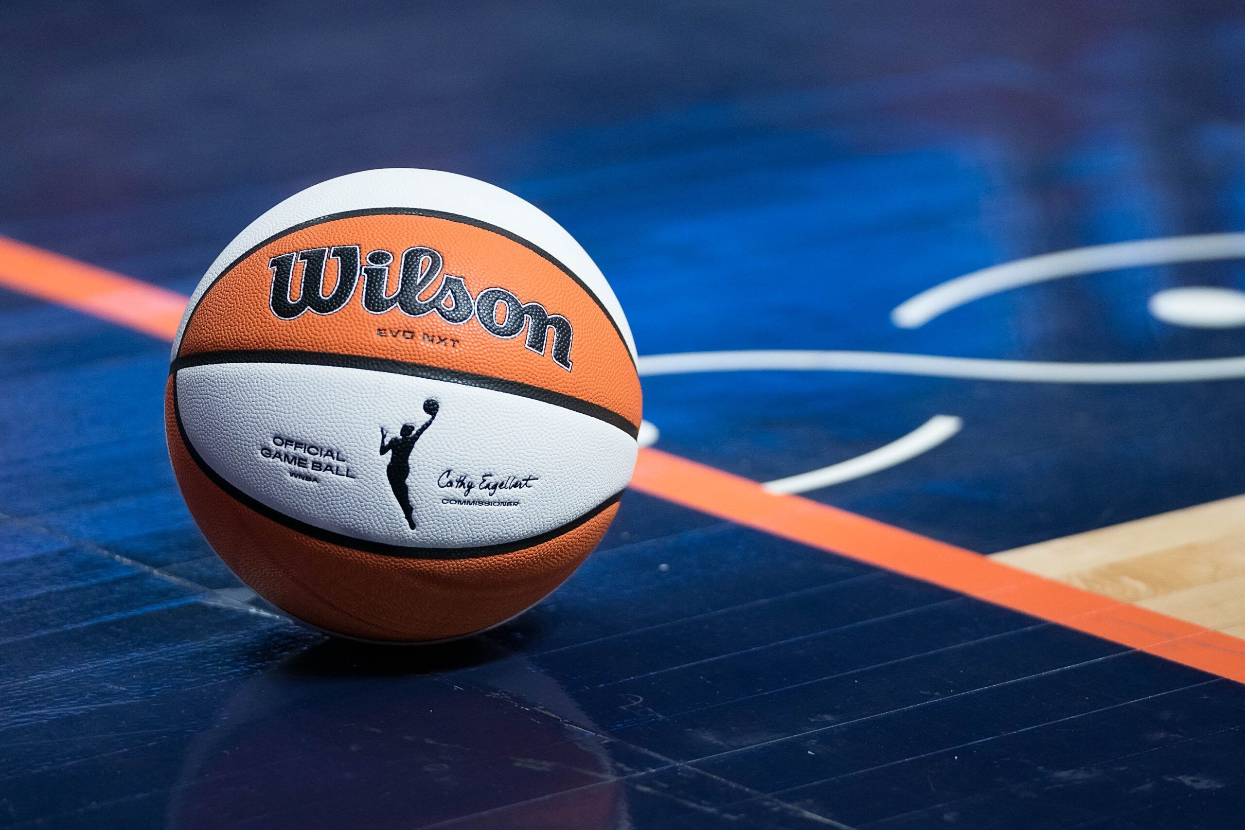 An orange and white Wilson basketball with the WNBA logo on it sits on the blue Connecticut Sun basketball court.
