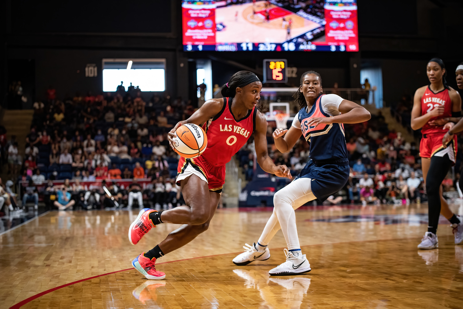 Las Vegas Aces wing Jackie Young drives to the rim from the slot, as Washington Mystics off-ball guard Ariel Atkins stands behind and beside her, trying to turn around and follow Young donwhill