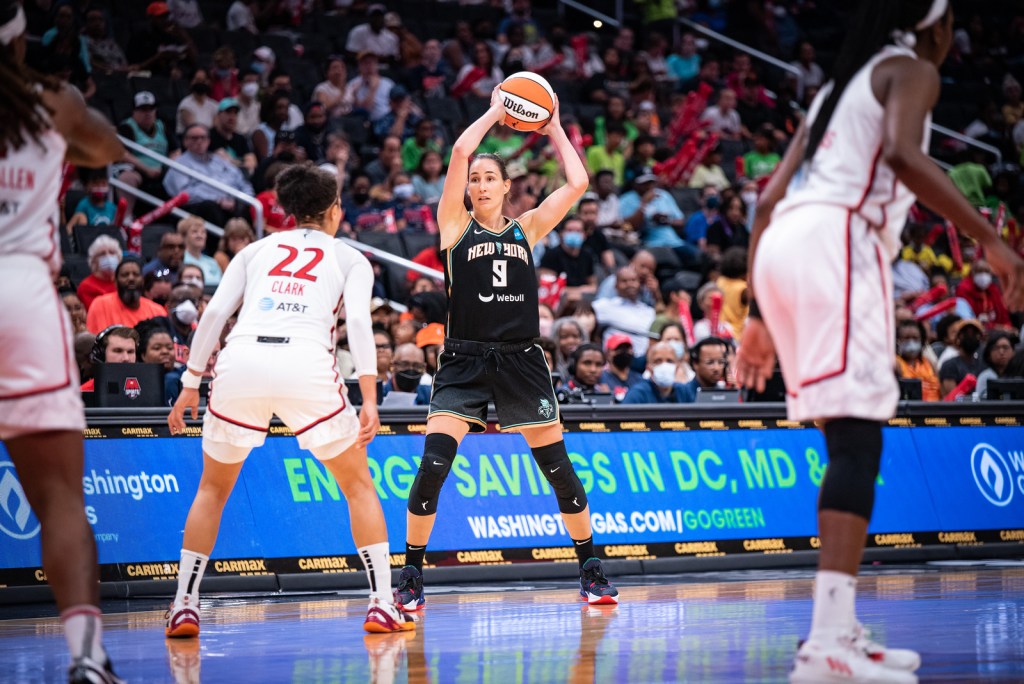 New York Liberty combo forward Rebecca Allen stands at the slot holding the ball above her head while she scans upcourt, as Washington Mystics off-ball guard Alysha Clark stands in front of her to defend