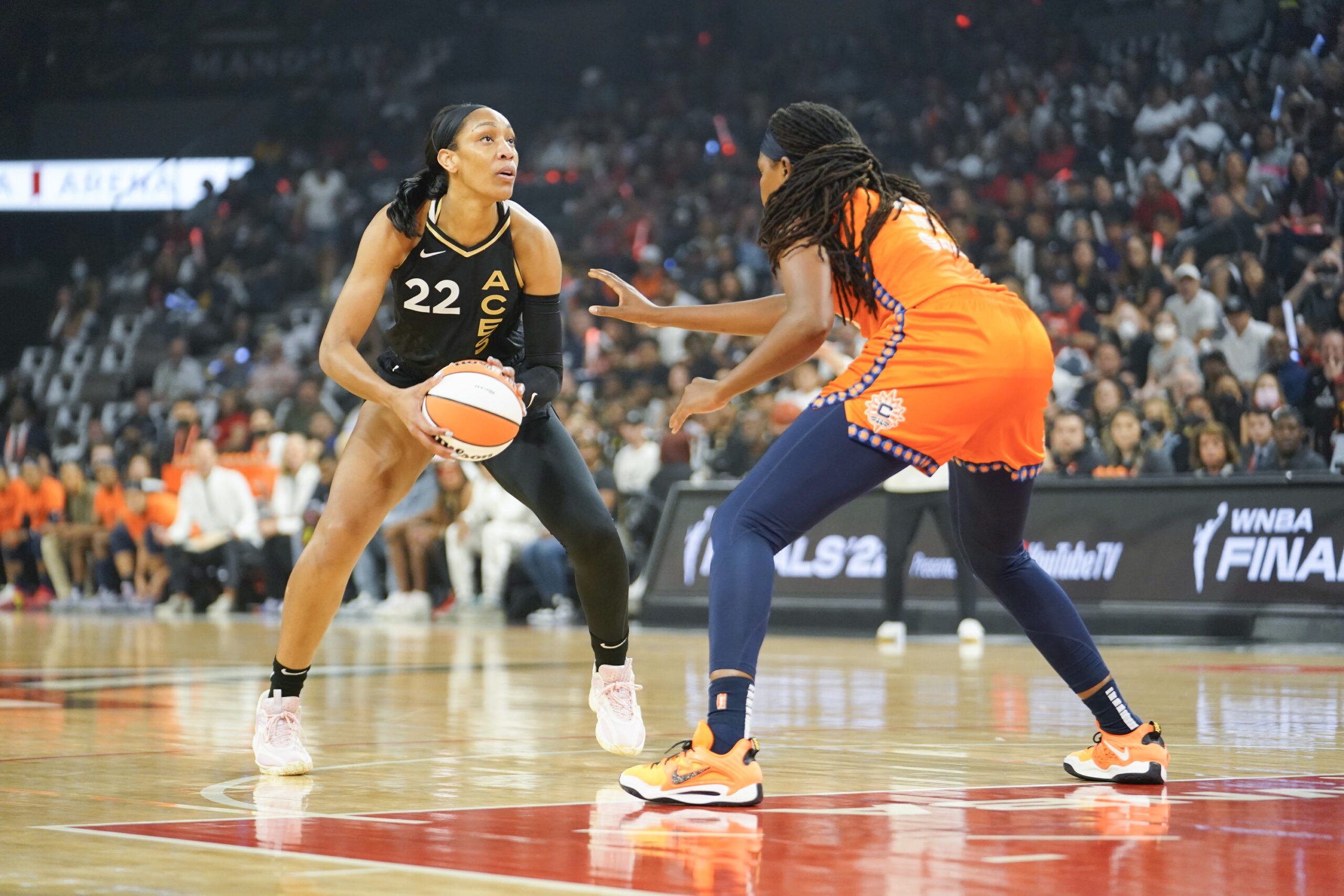 Aces center A'ja Wilson (22) gathers the ball at the top of the key while Connecticut Sun big Jonquel Jones (35) defends, her right arm outstretched.