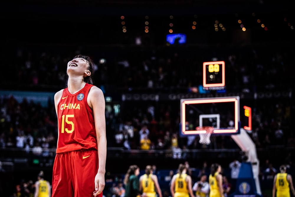 China's Han Xu (15) looks up towards the ceiling with a smile. The shot clock on the basket behind her reads zero, as Australian players walk away towrads the bench.