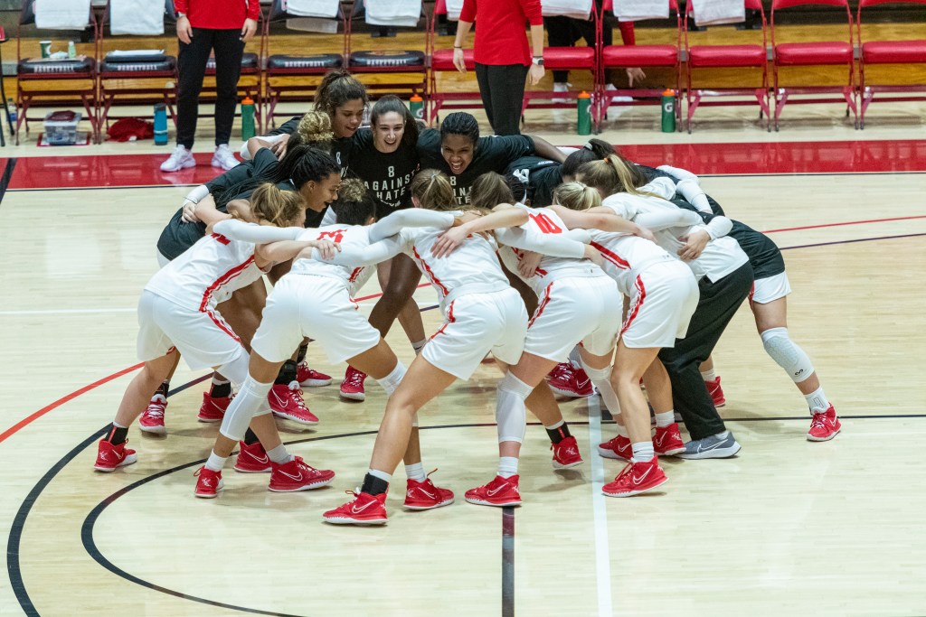 Cornell players in white game jerseys and black warm-up shirts huddle.