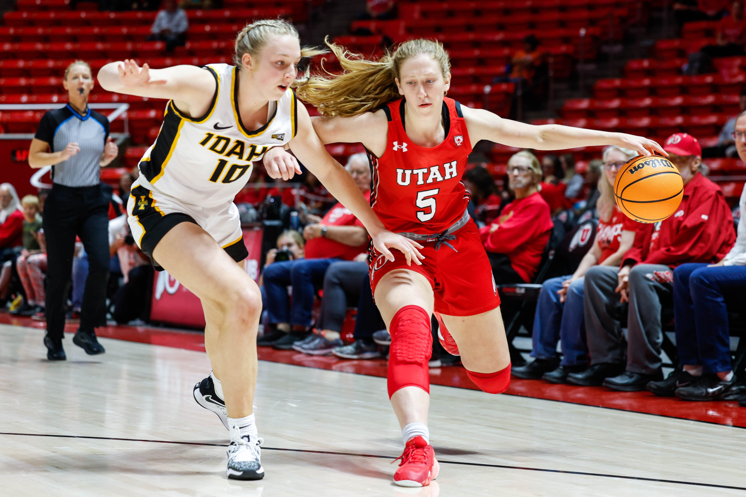 Utah guard Gianna Kneepkens dribbles the ball on the perimeter with her left hand, using her body and her right arm to fend off an Idaho defender.