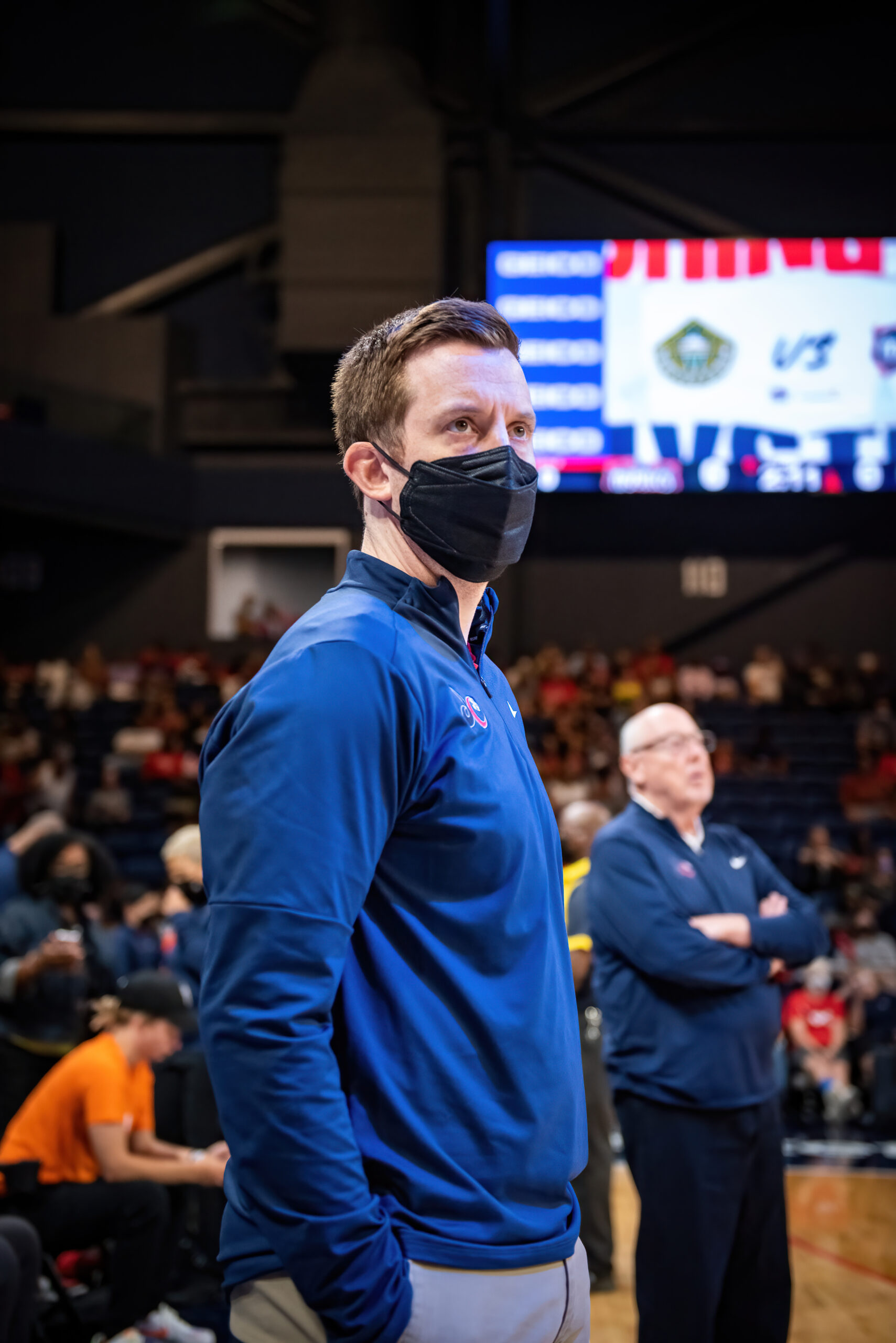 Then-Washington Mystics associate head coach Eric Thibault watches the game from the sideline with his hands at his sides. His father and then-head coach Mike Thibault is in the background with his arms crossed.