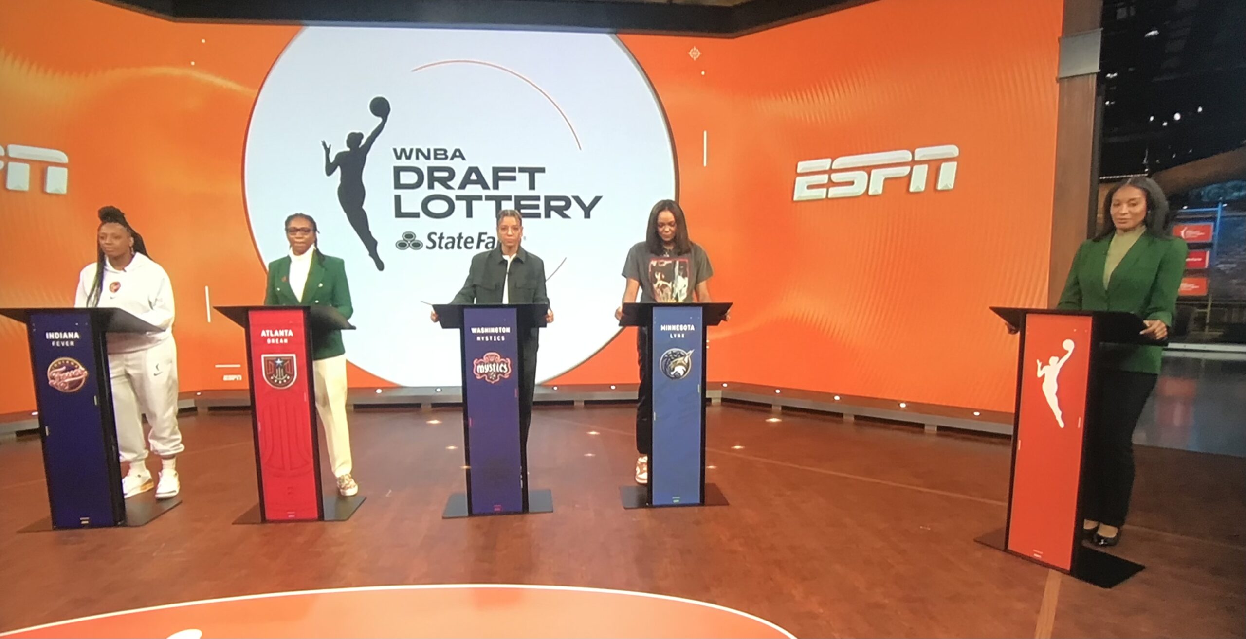 Representatives from the four teams in the 2023 WNBA draft lottery, including Washington Mystics point guard Natasha Cloud (third from left), stand behind podiums and await their fate.