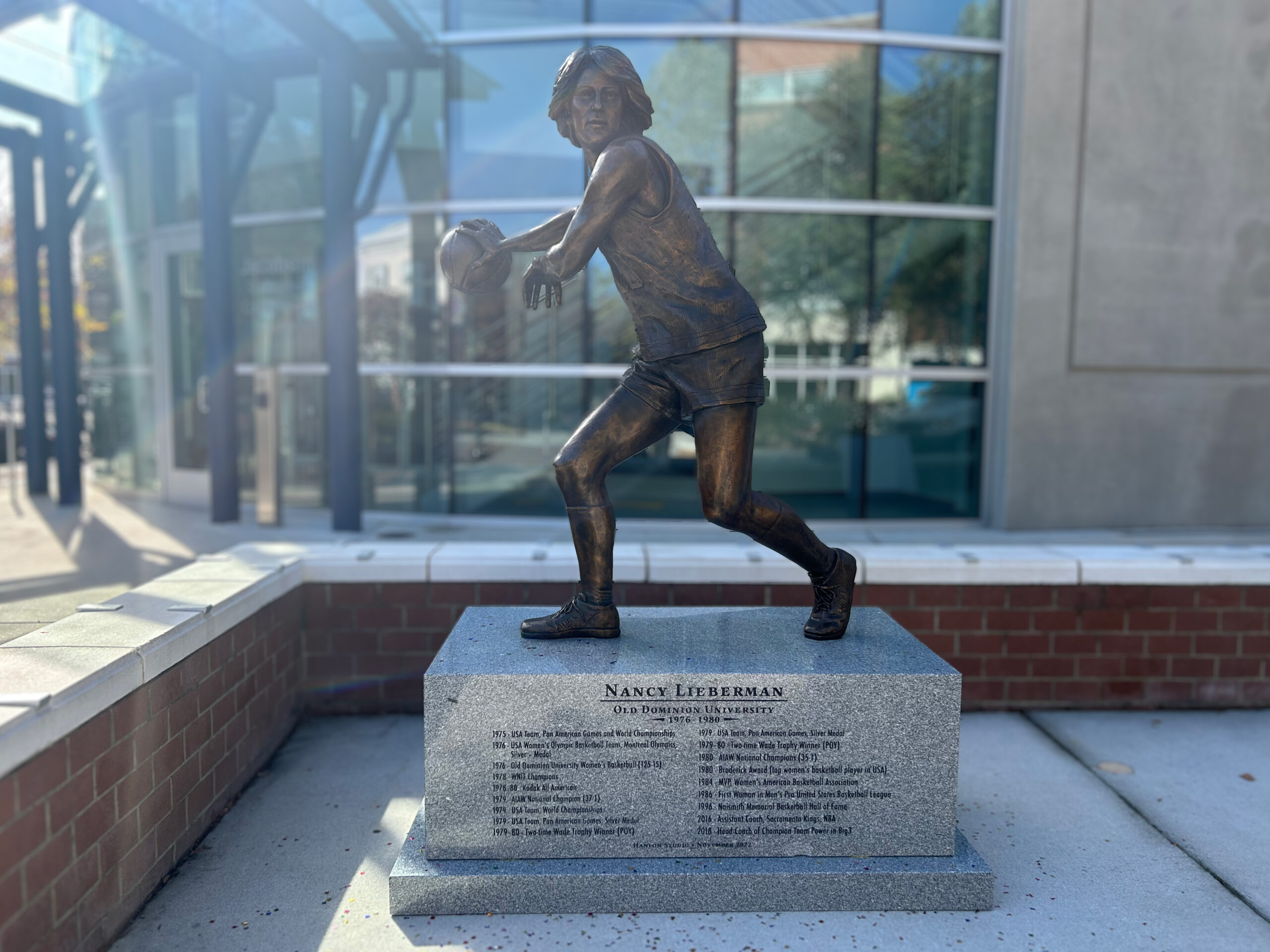 Nancy Lieberman statue at Old Dominion. The statue is bronze. Nancy Lieberman reaches her left arm over while holding the ball in her right hand.
