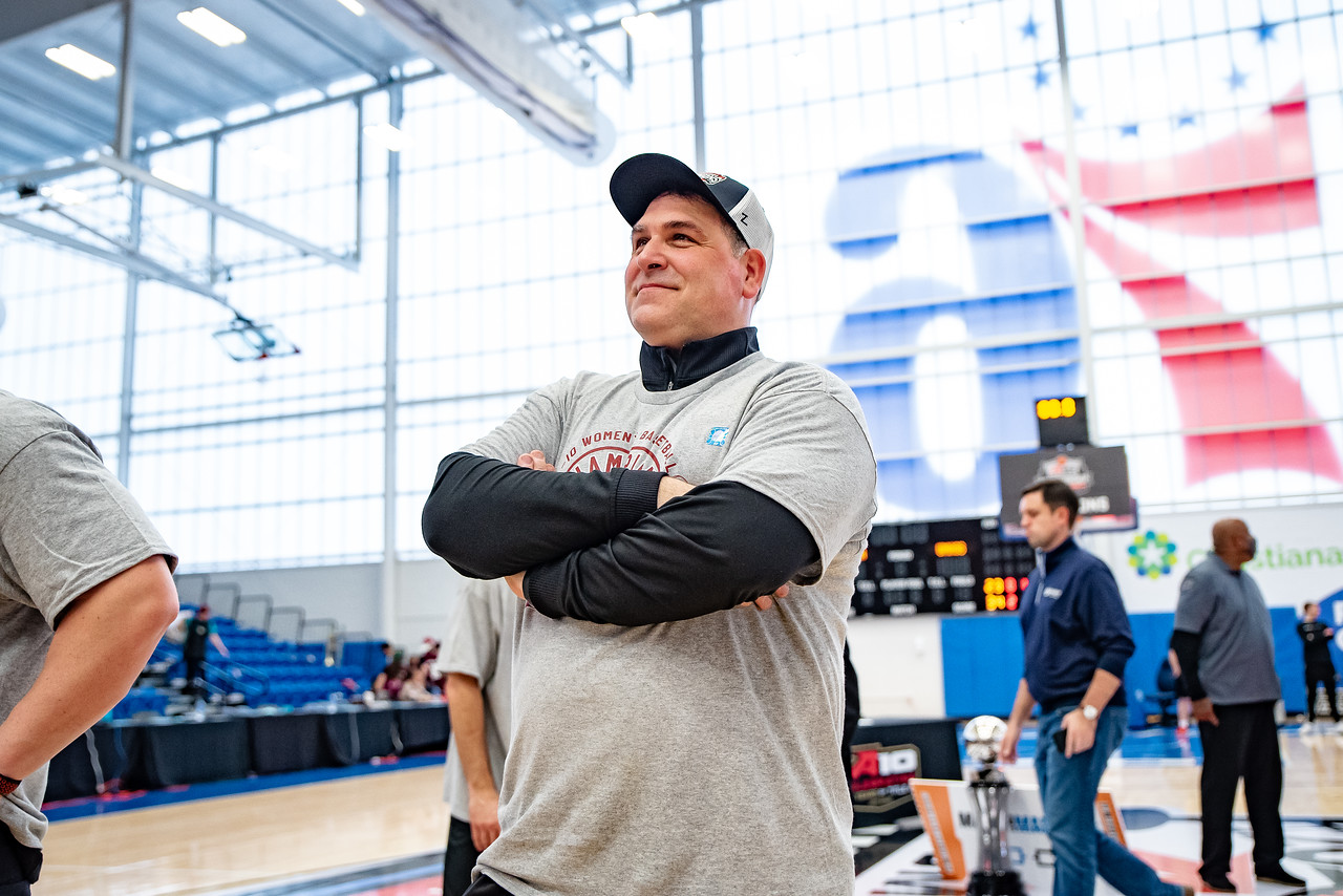 UMass head coach Tory Verdi watches his players cut down the net after winning the A-10 championship on March 6, 2022 while wearing a championship hat and shirt