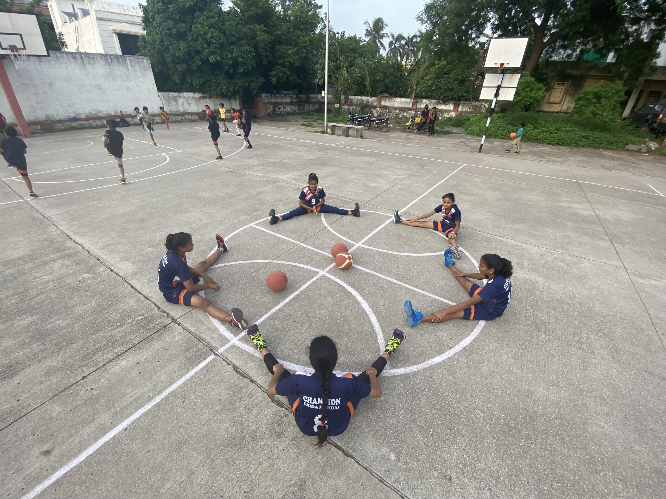 Photo of youth basketball players circled up on an outdoor basketball court in India.