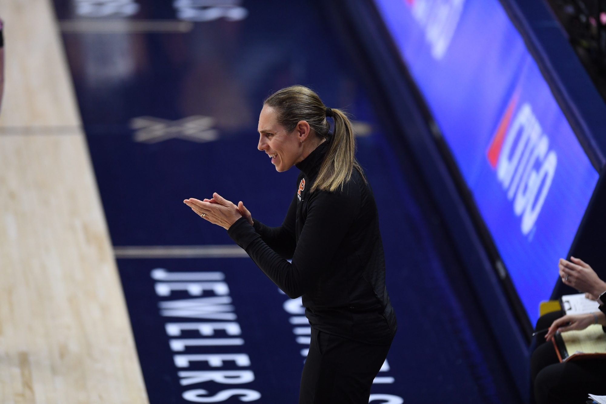 Princeton head coach Carla Berube is shown in profile, smiling and clapping during a game against UConn.