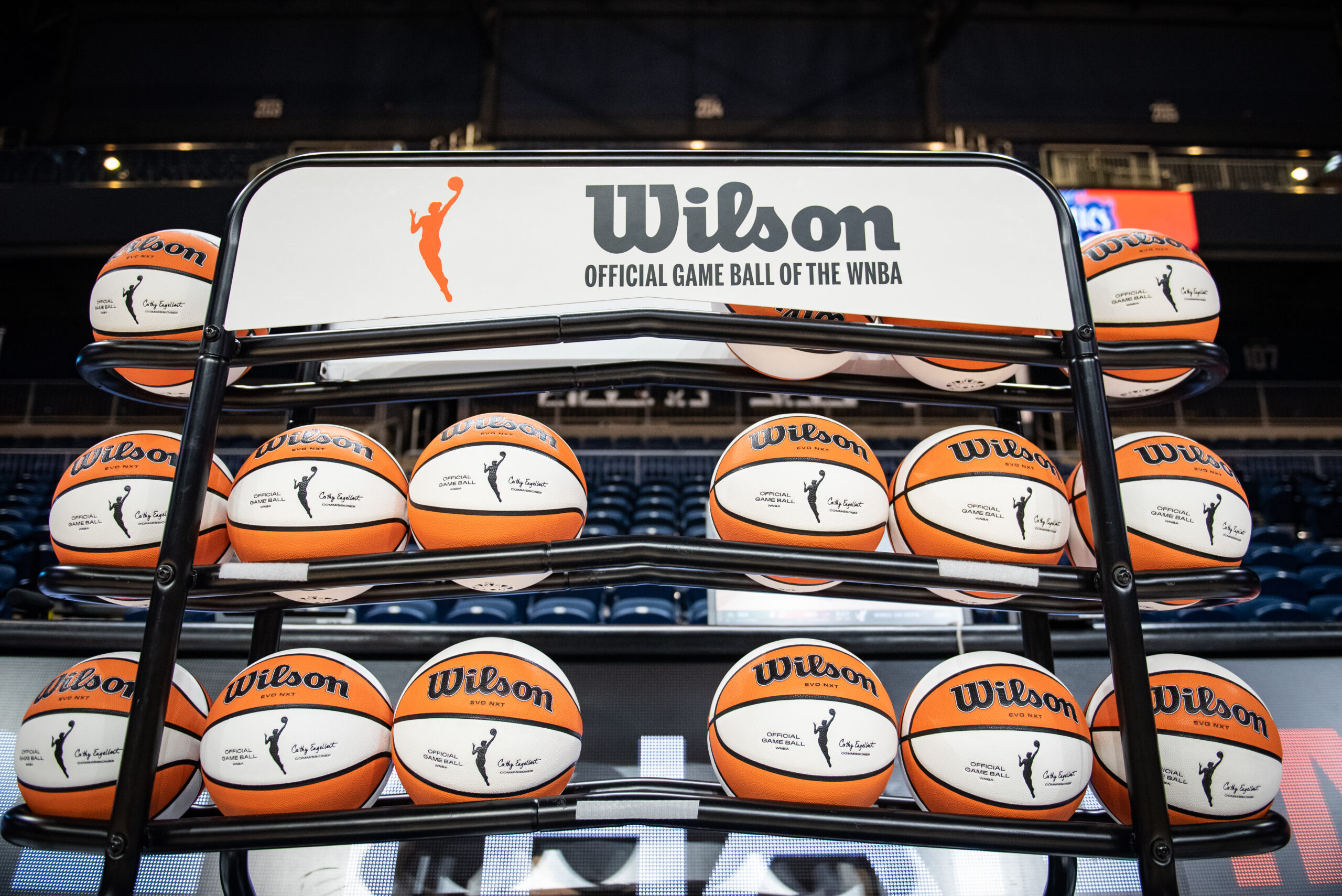 More than a dozen orange and white WNBA basketballs sit on a rack.