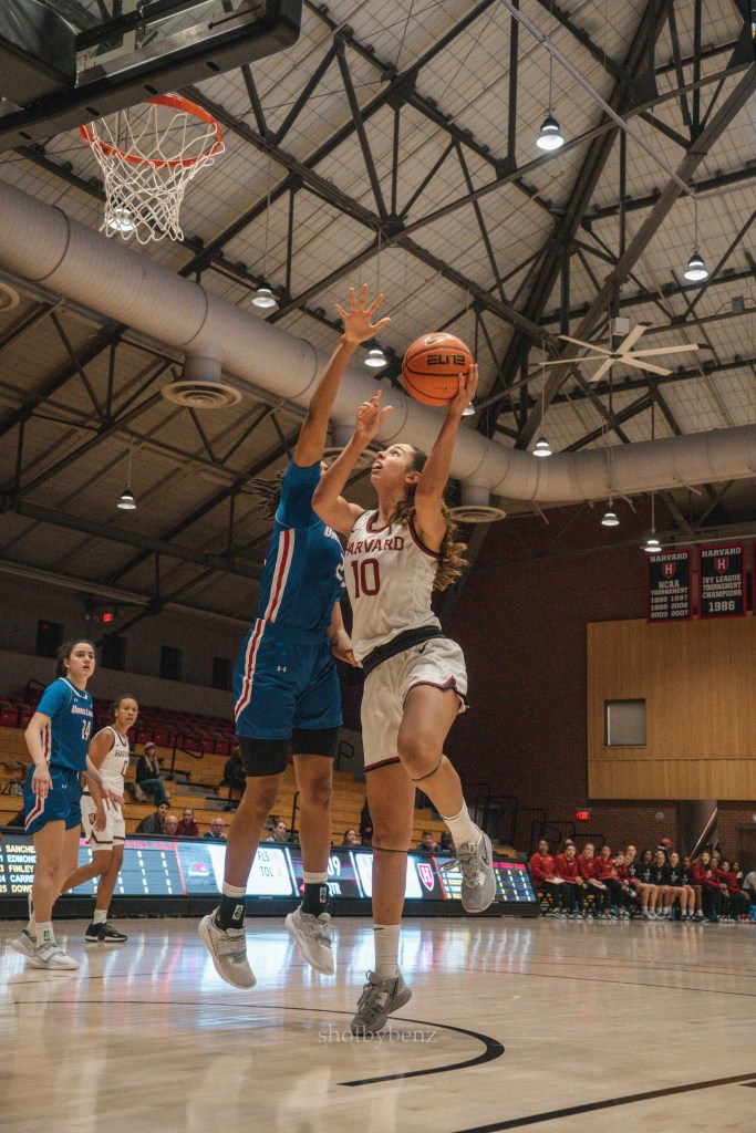Harvard guard Elena Rodriguez attempts a left-handed layup as a UMass Lowell defender contests with their right hand and body.