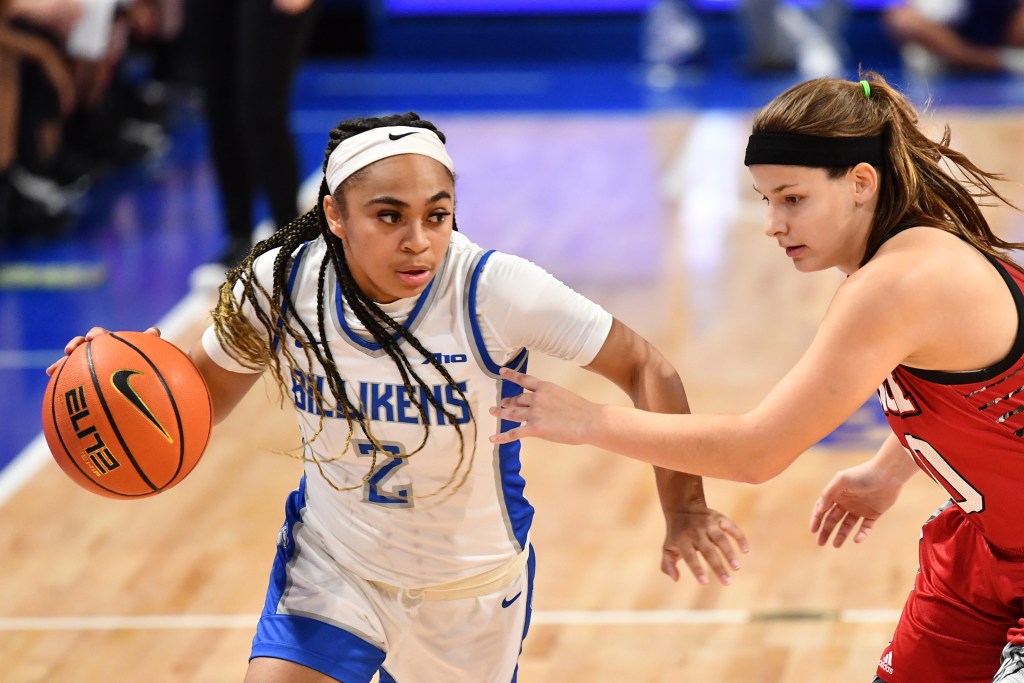 Camree Clegg (white and blue uniform) dribbles around her defender (red and black uniform) against SIUE