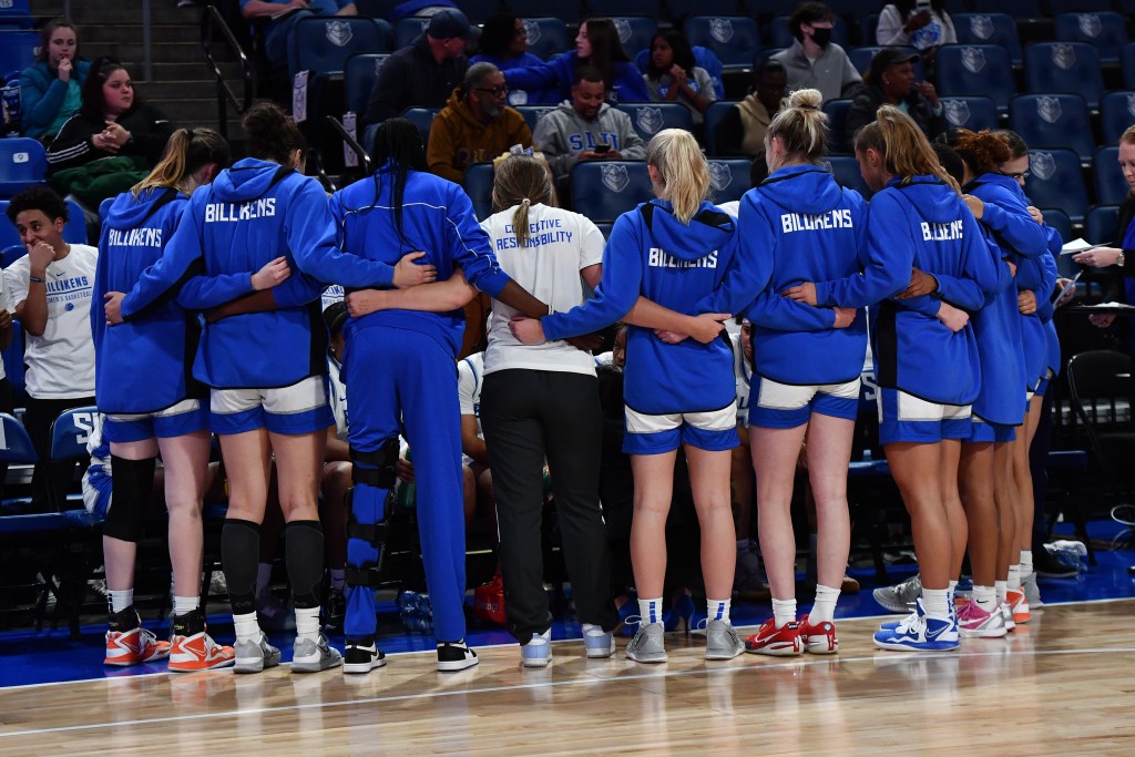 Saint Louis Billikens huddle during a game against SIUE wearing white uniforms and blue warmups.