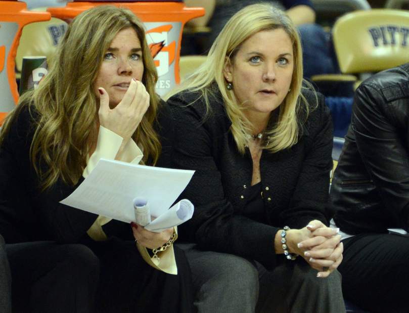 Pittsburgh associate head coach Kathy McConnell-Miller (left) and head coach Suzie McConnell Serio gaze out at the court. McConnell-Miller holds several pieces of paper, while McConnell Serio's hands are clasped in front of her.