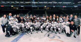 Yale women's hockey team poses on ice in Yale Blue and White jerseys.