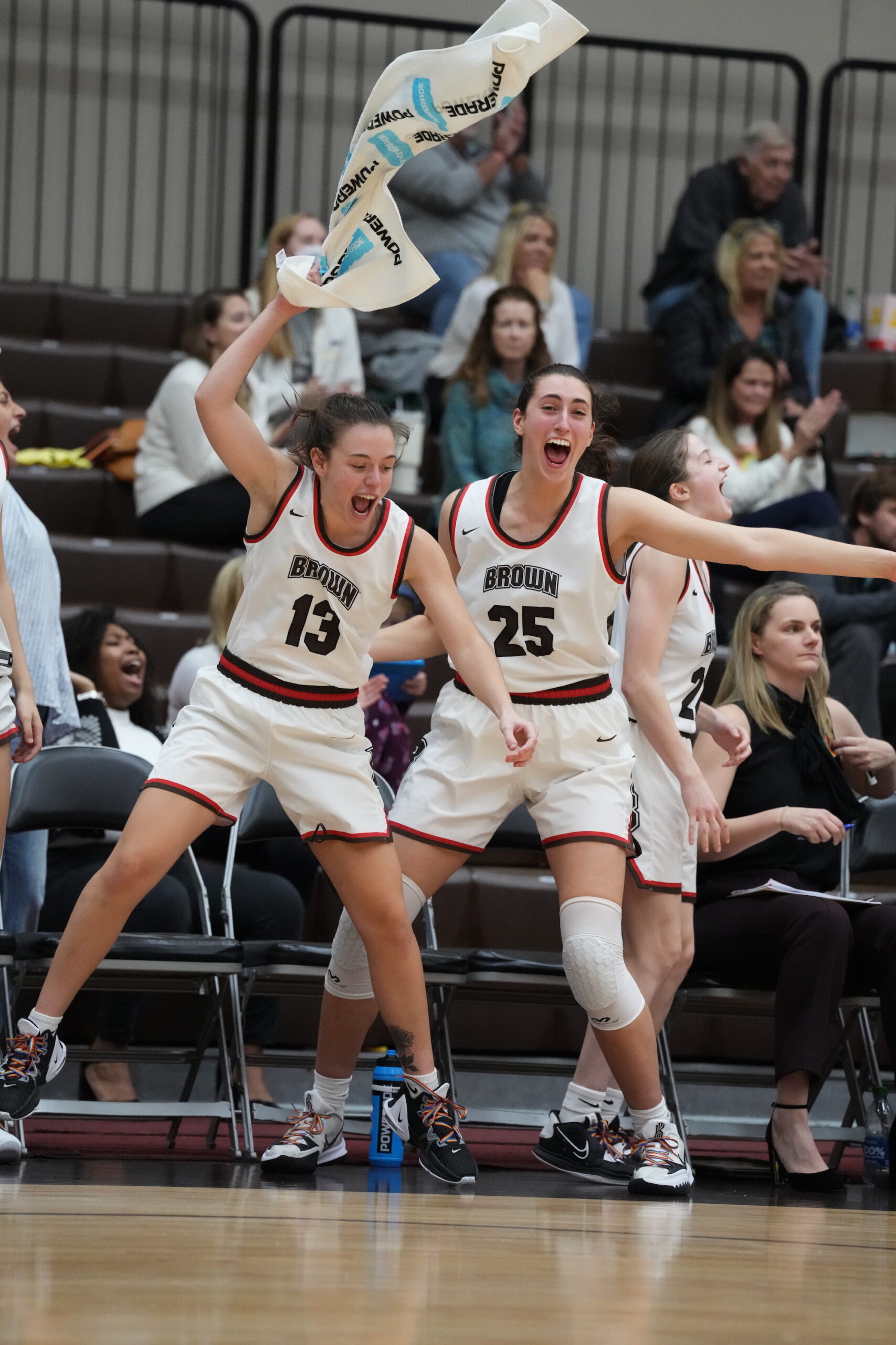 Brown guard Charlotte Jewell and center Gianna Aiello yell in delight on the bench, and Jewell swings a white towel above her head with her right hand.