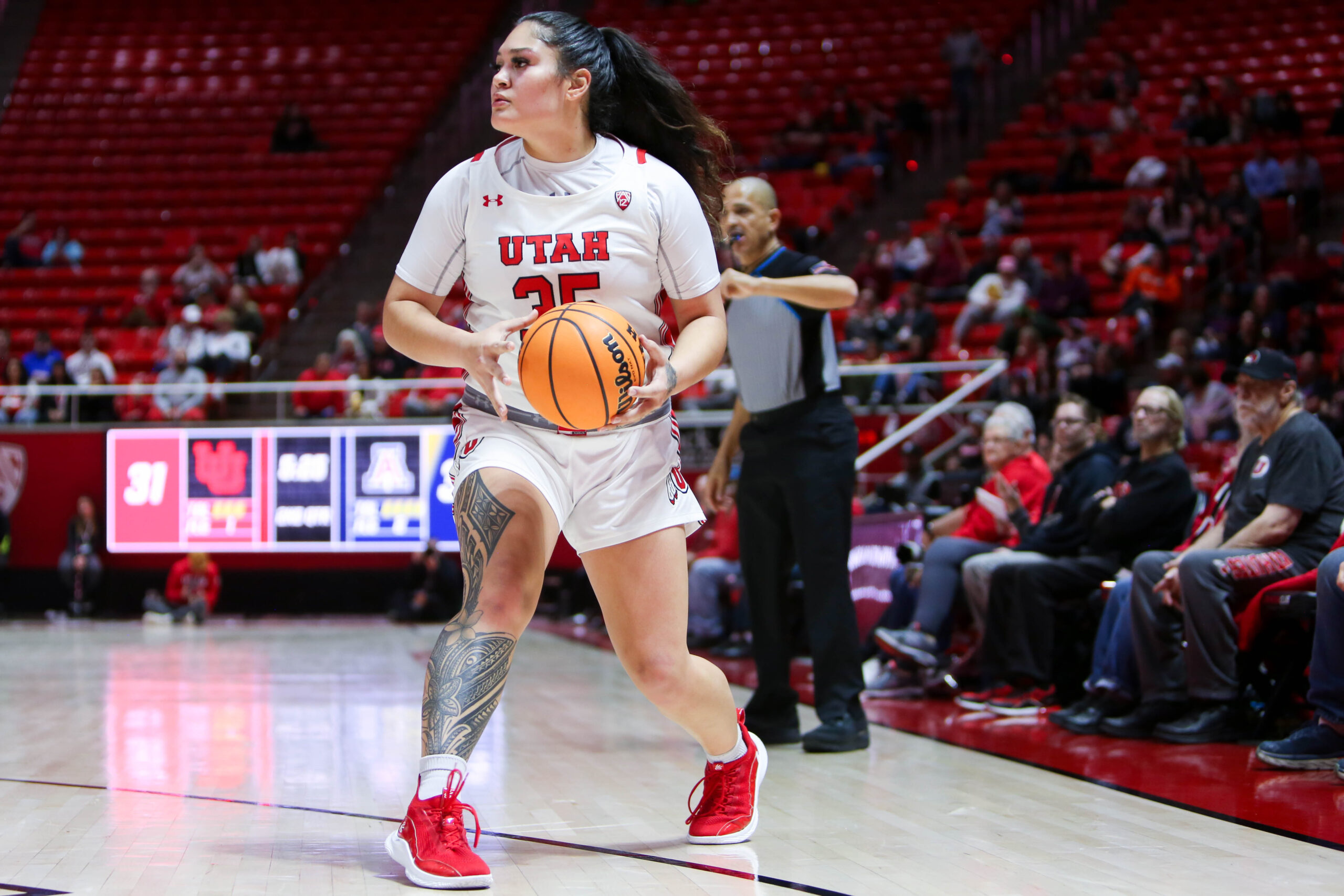 Utah forward Alyssa Pili (35) holds the ball and looks to pass during a game at the Huntsman Center. A referee stands and signals behind her.