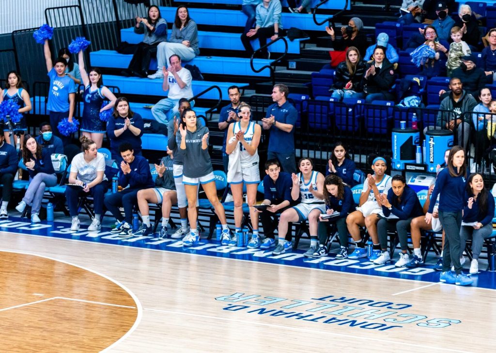 Sienna Durr stands on the sideline and leans forward, clapping as she looks down the court.
