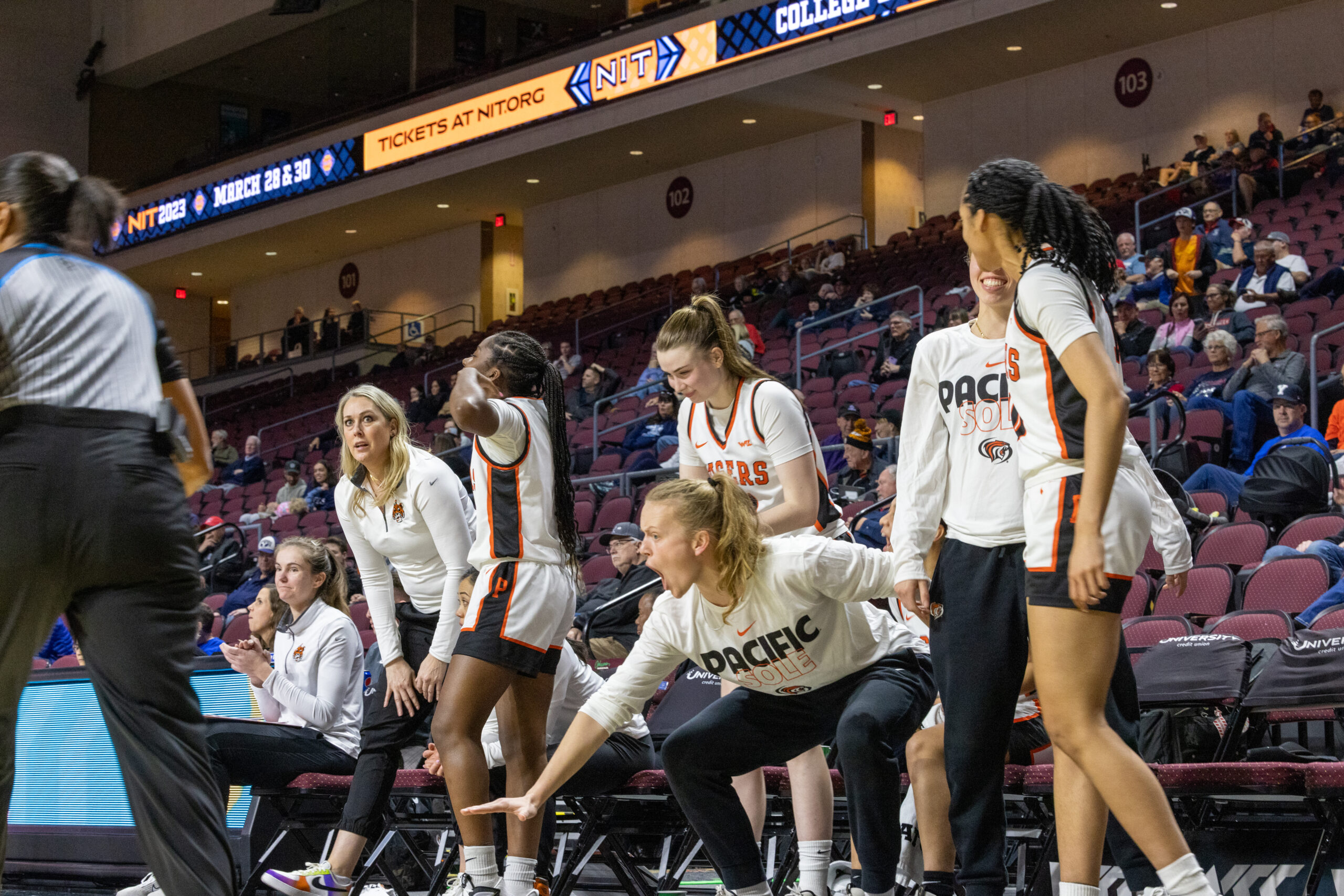 Pacific's bench celebrates. One player squats, yells and puts her right hand low to the ground.