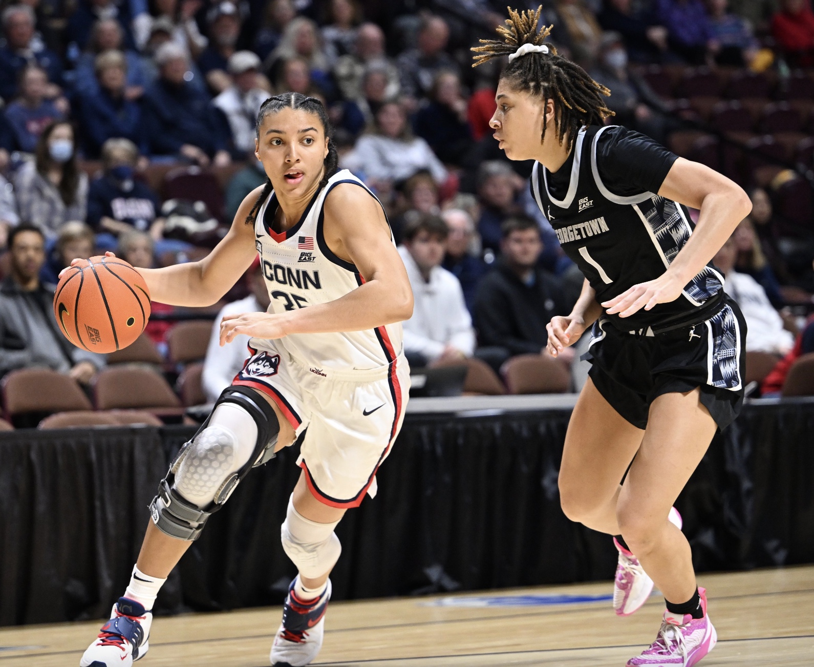 UConn's Azzi Fudd drives to the basket against Georgetown's Kelsey Ransom. Fudd has the ball in her right hand, and she is pictured in the UConn home red, white and blue jersey. She has a bulky knee brace on her right knee. Guarding her is Ransom in the Georgetown black and white away jersey.