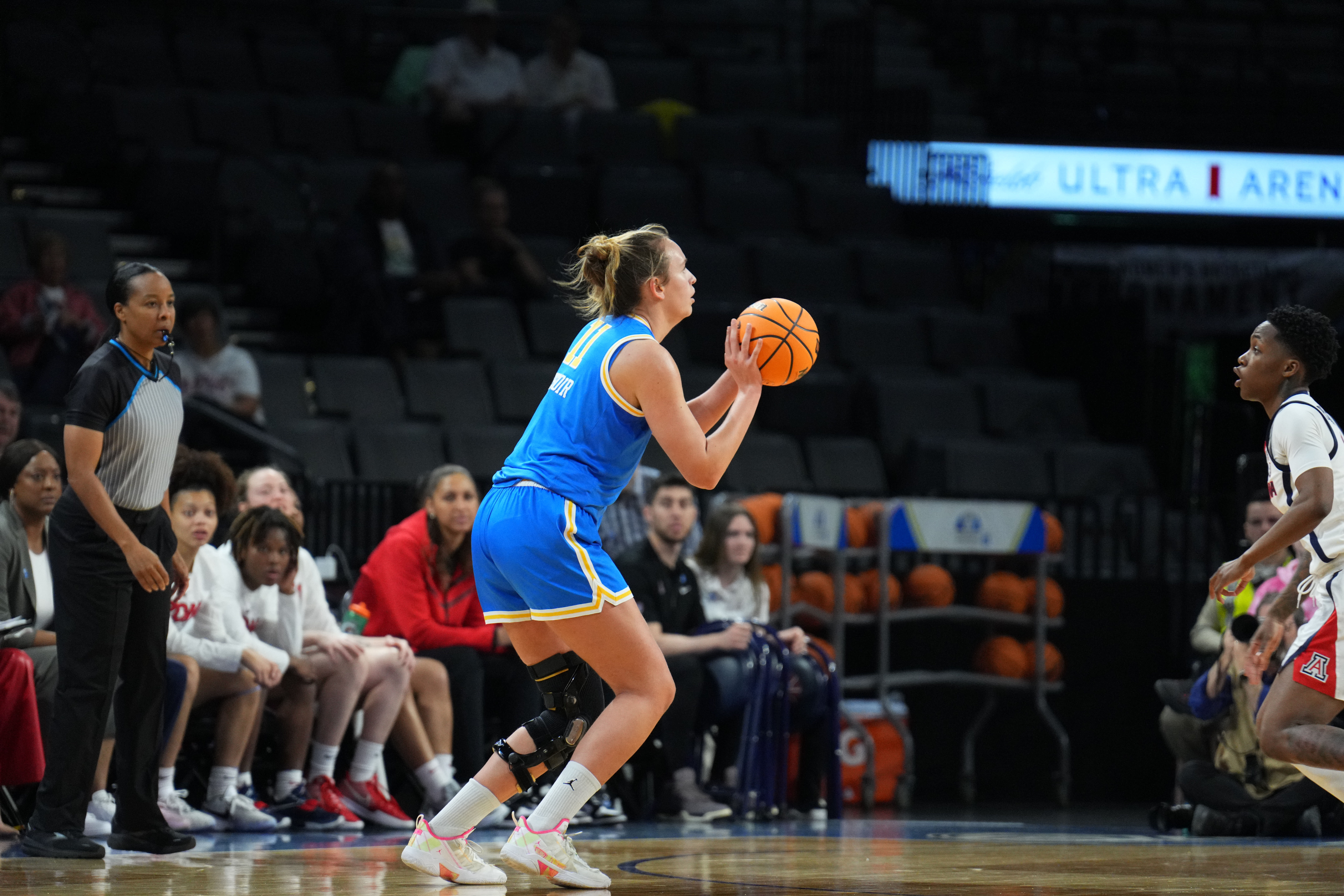 UCLA forward Emily Bessoir is shown in profile, preparing to take an open jump shot. An Arizona defender is barely visible in the photo, several steps from Bessoir with her hands down.