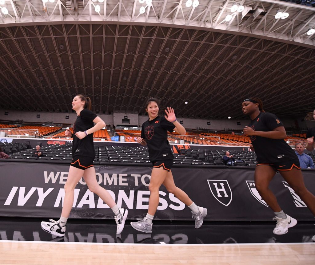 Princeton guards Maggie Connolly, Kaitlyn Chen and Adaora Nwokeji run laps around the perimeter of the court. Connolly and Nwokeji look straight ahead, but Chen smiles and waves at the camera.