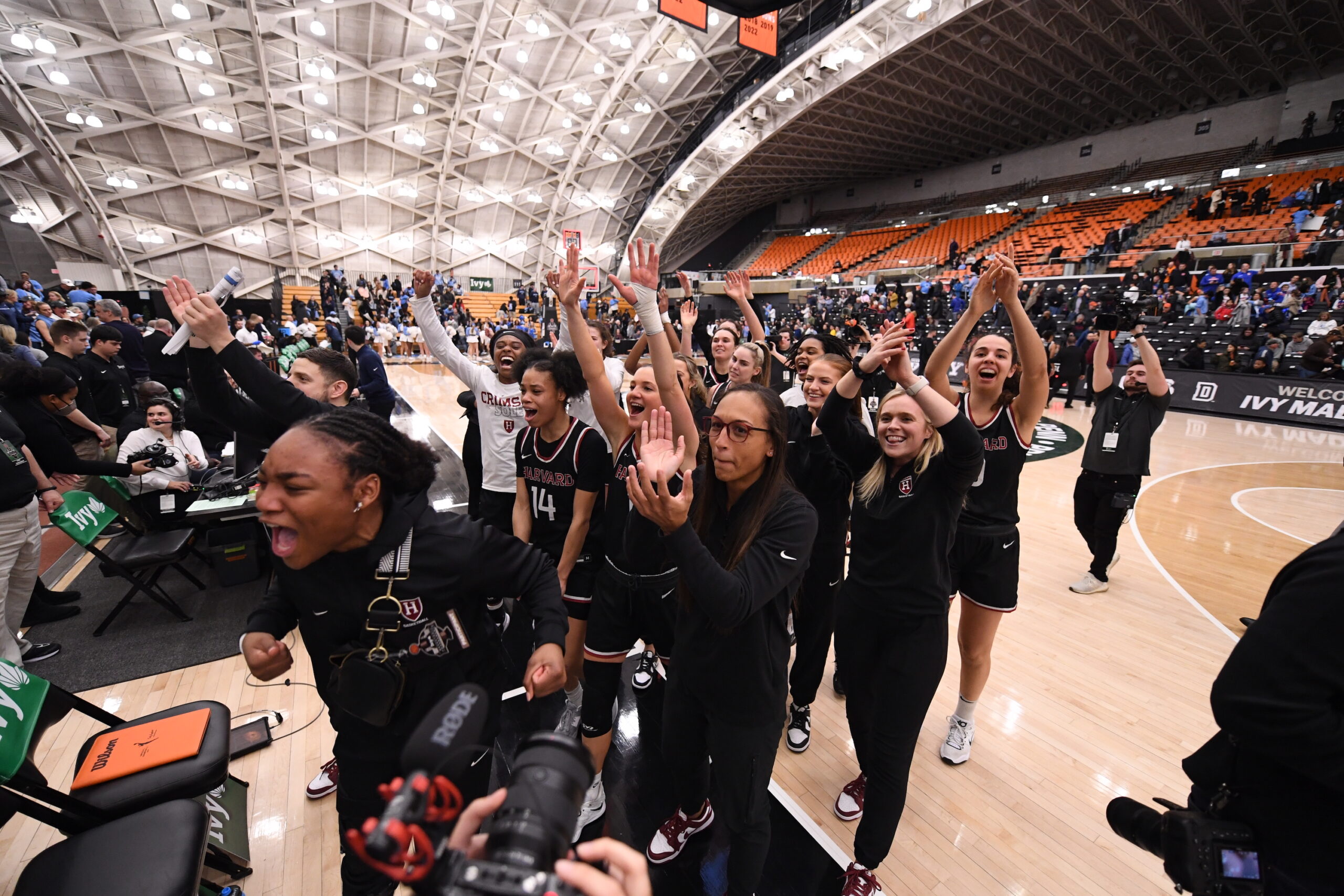 Harvard players and coaches yell and clap in celebration in front of their supporters section at the 2023 Ivy League Tournament.