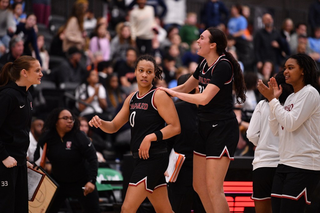 Harvard freshman forward Katie Krupa jumps in the air, with her hands on the shoulders of senior guard McKenzie Forbes as they celebrate.