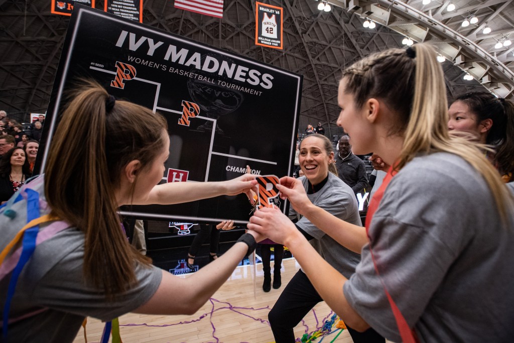 Princeton head coach Carla Berube and senior guards Maggie Connolly and Julia Cunningham put a sticker of an orange and black Princeton "P" in the champions slot on a black Ivy League Tournament bracket.