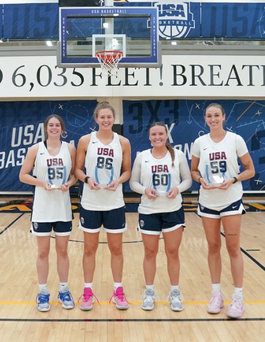 Creighton women's basketball players Lauren Jensen, Morgan Maly, Molly Mogensen and Emma Ronsiek stand in Team USA pinnies while holding the USA Basketball 3x3 championship trophy.