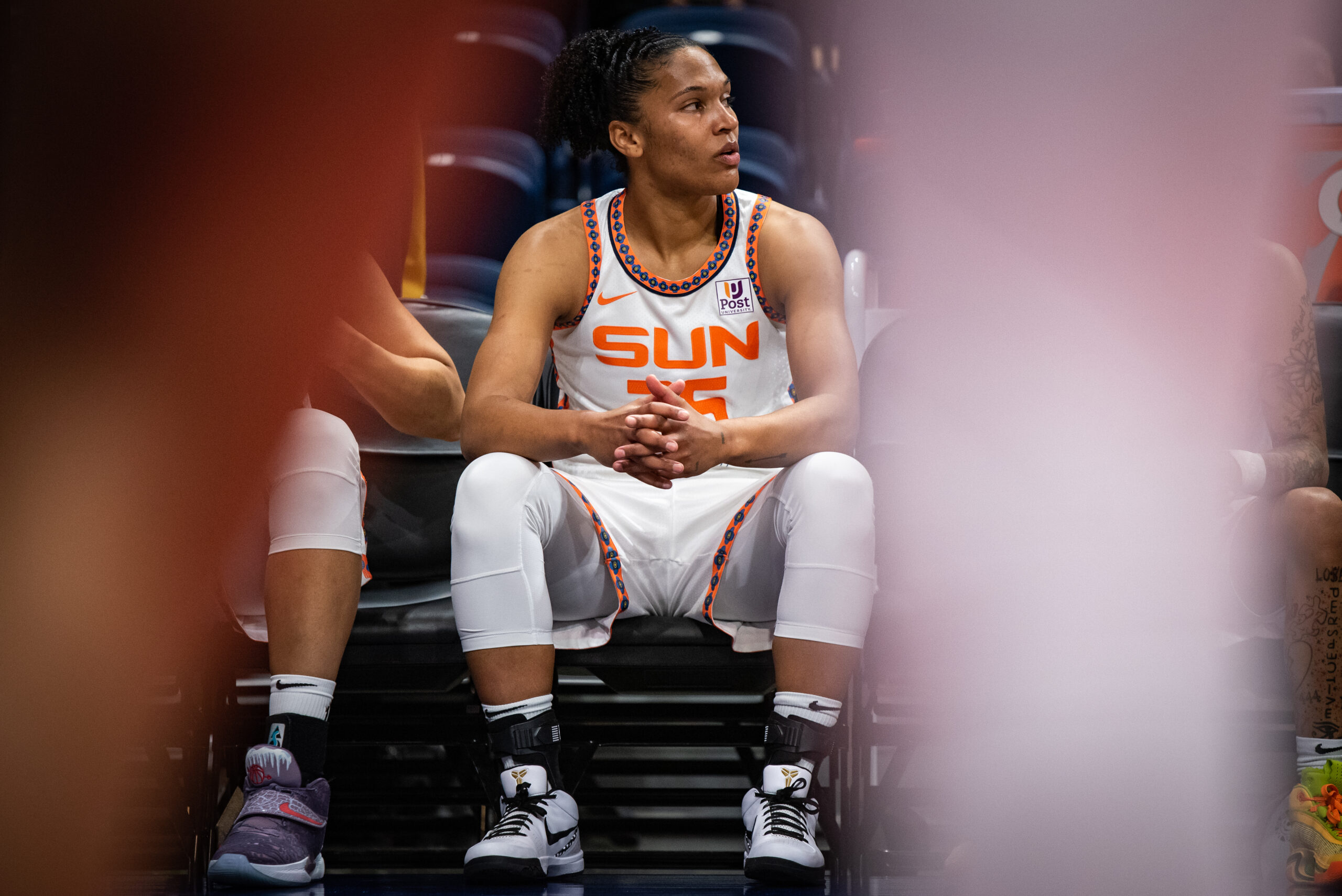 Connecticut Sun forward Alyssa Thomas sits on the bench alertly, with her hands clasped in front of her.