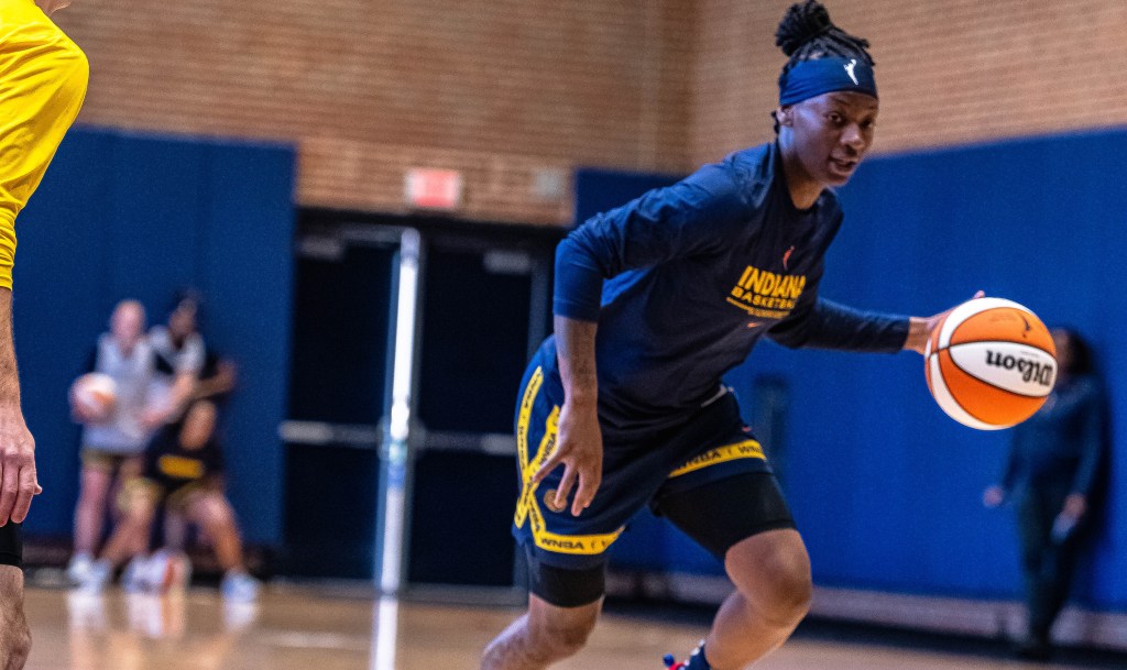 Indiana Fever point guard dribbles the ball to her left with her left hand.