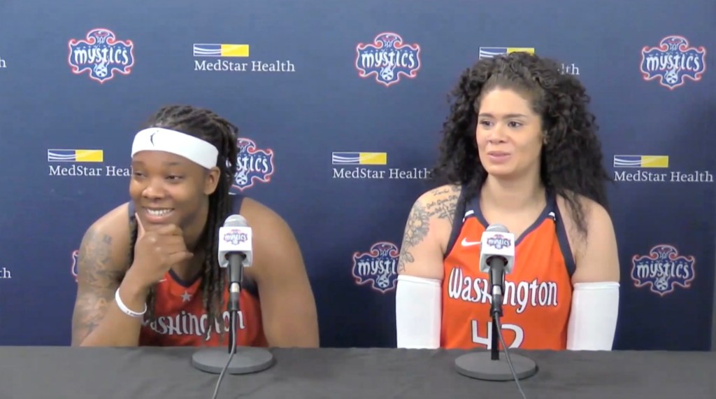 Washington Mystics forward Myisha Hines-Allen and center Amanda Zahui B. smile as they sit at the podium talking to reporters. A backdrop dotted with Mystics and MedStar Health logos is behind them.