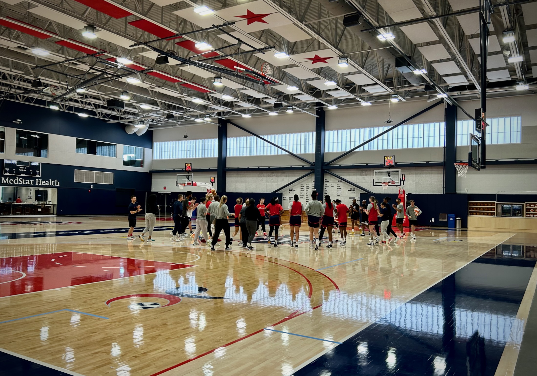 Washington Mystics players and staff stand in a loose circle at halfcourt and talk at the end of a practice.