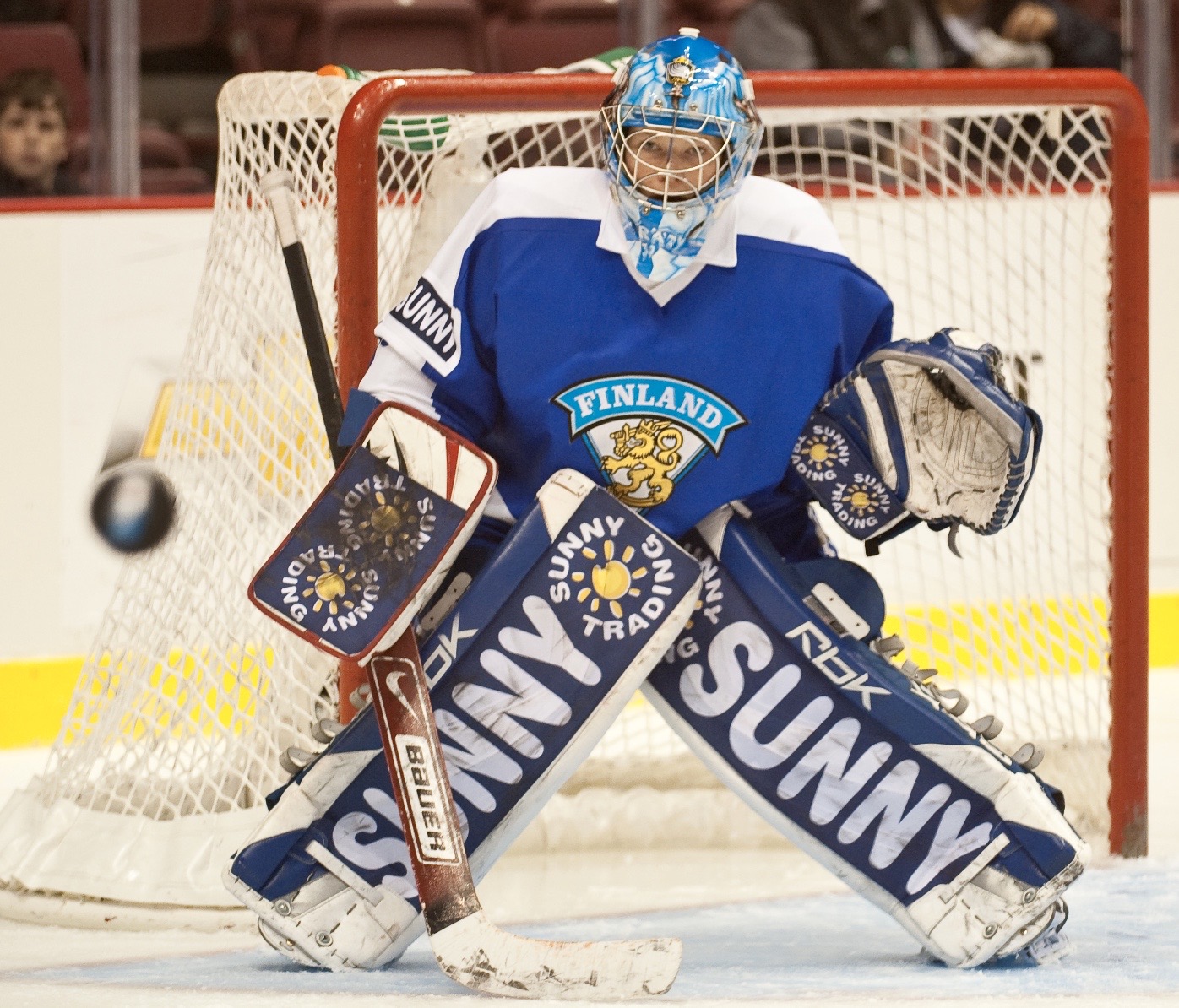 Goalie Noora Räty is positioned in front of the net wearing Finnish hockey gear.