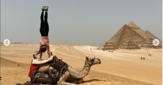 Sandra Elsadek does a handstand on a camel that is sitting in the sand in the desert.