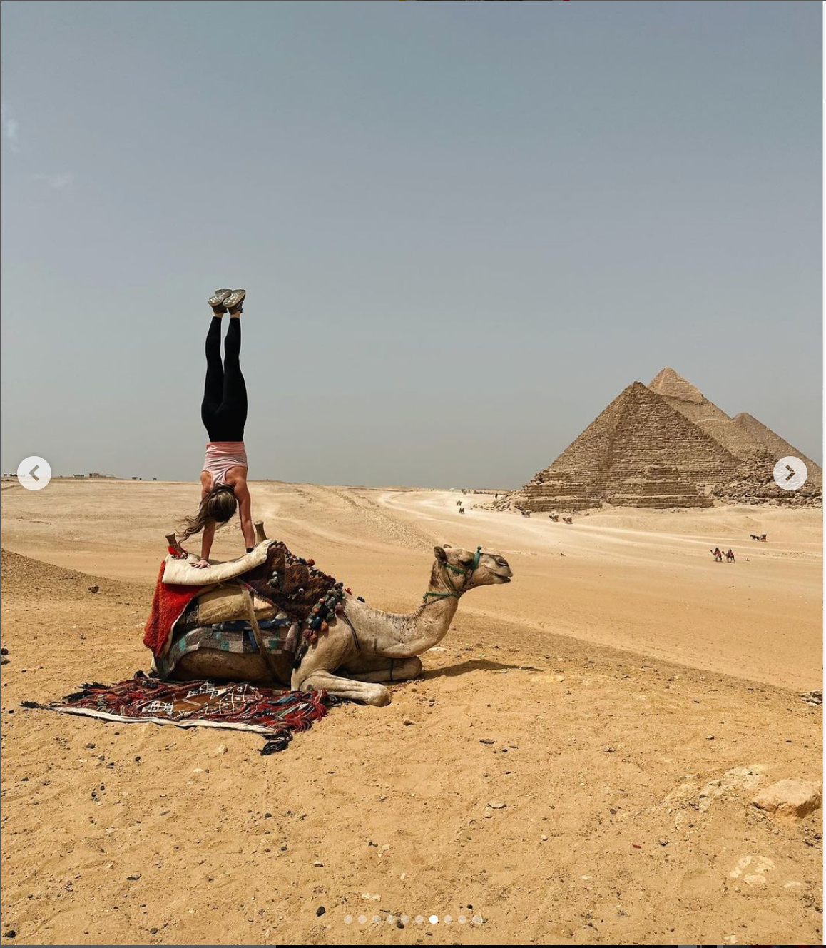 Sandra Elsadek does a handstand on a camel that is sitting in the sand in the desert.