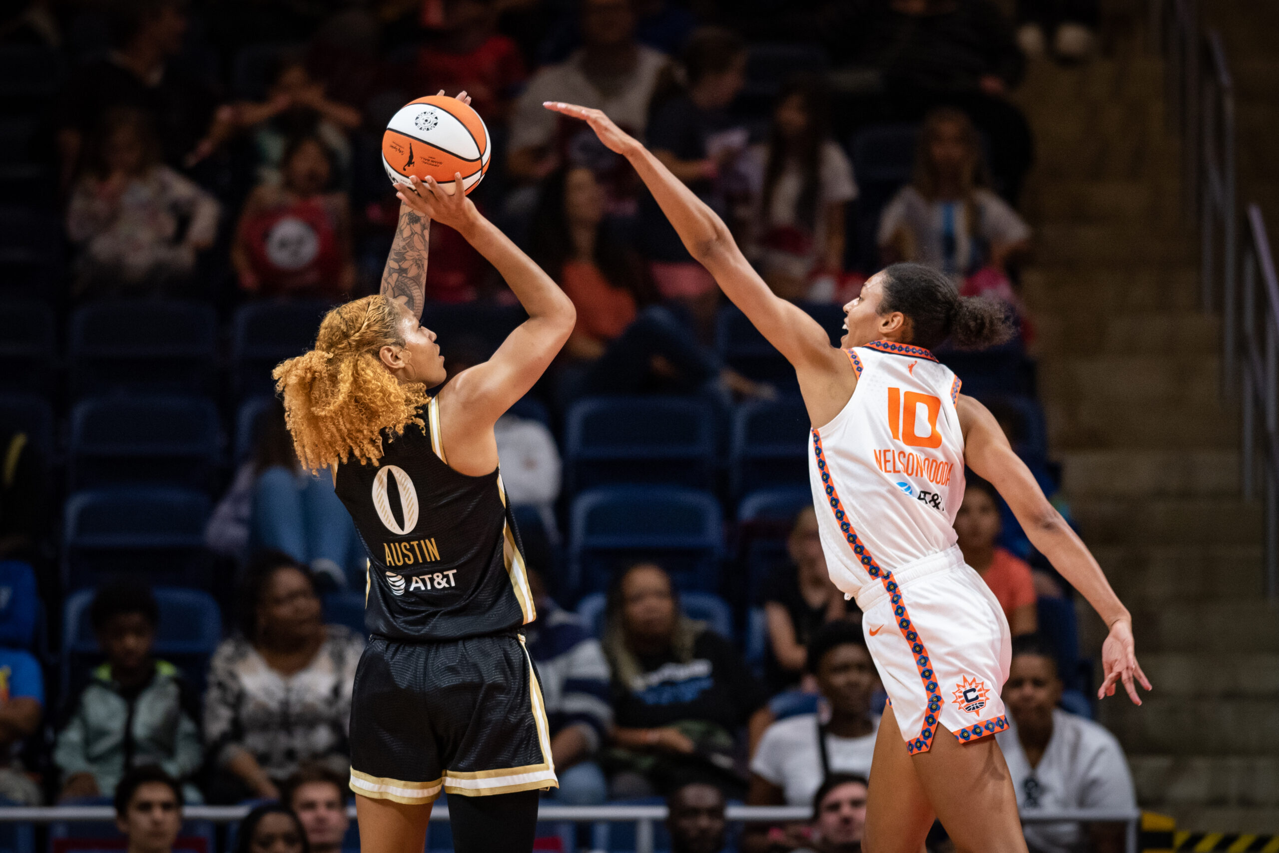 Washington Mystics center Shakira Austin holds the ball above her head as she shoots a jumper, while Connecticut Sun center Olivia Nelson-Ododa reaches toward her with an outstretch arm to try to contest the shot