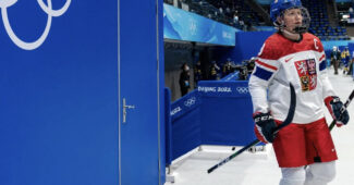 Czechia captain Alena Mills skates on the ice with Olympics symbol in the backdrop.
