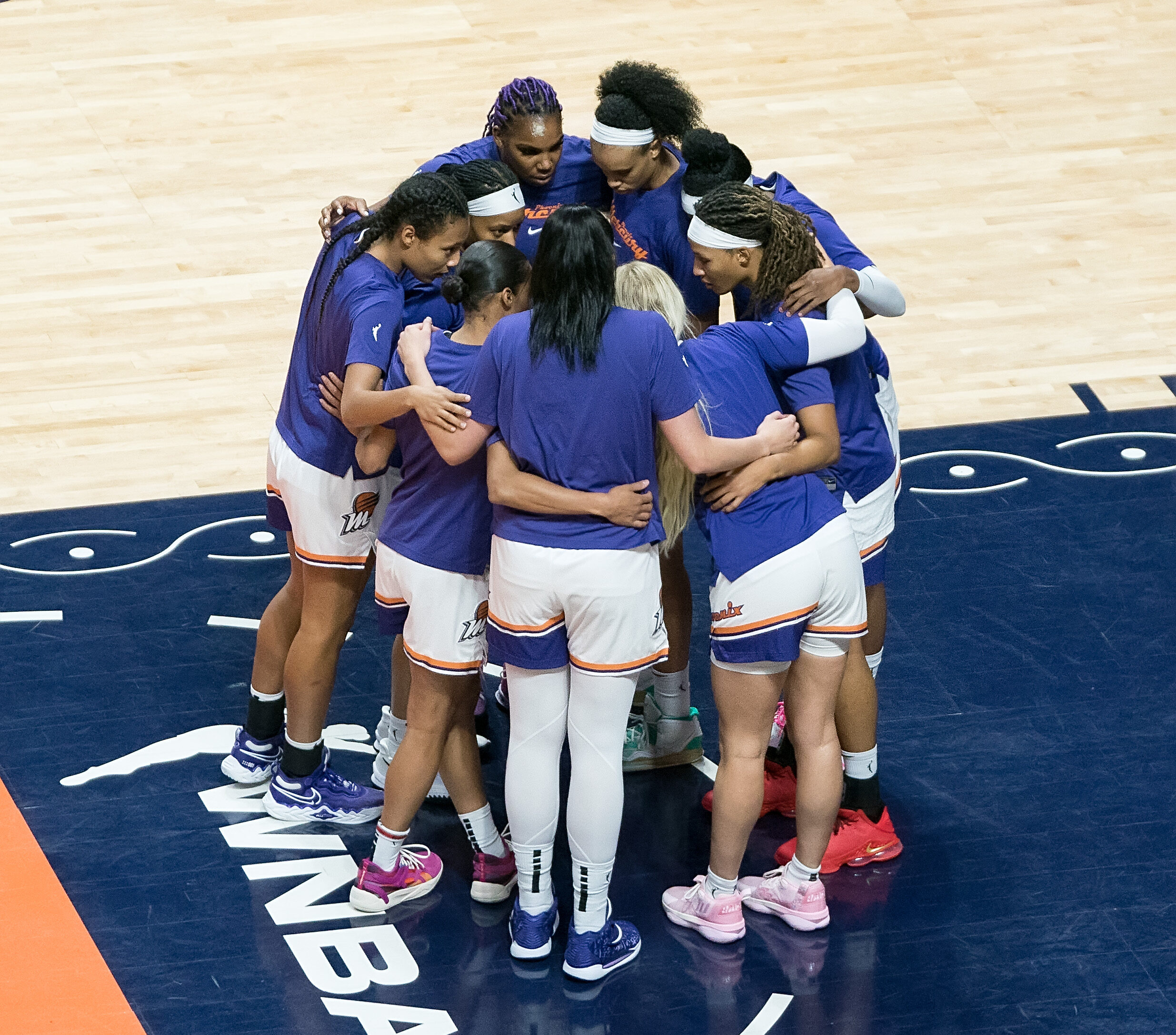 Nine Phoenix Mercury players form a tight huddle in the lane near the free-throw line.