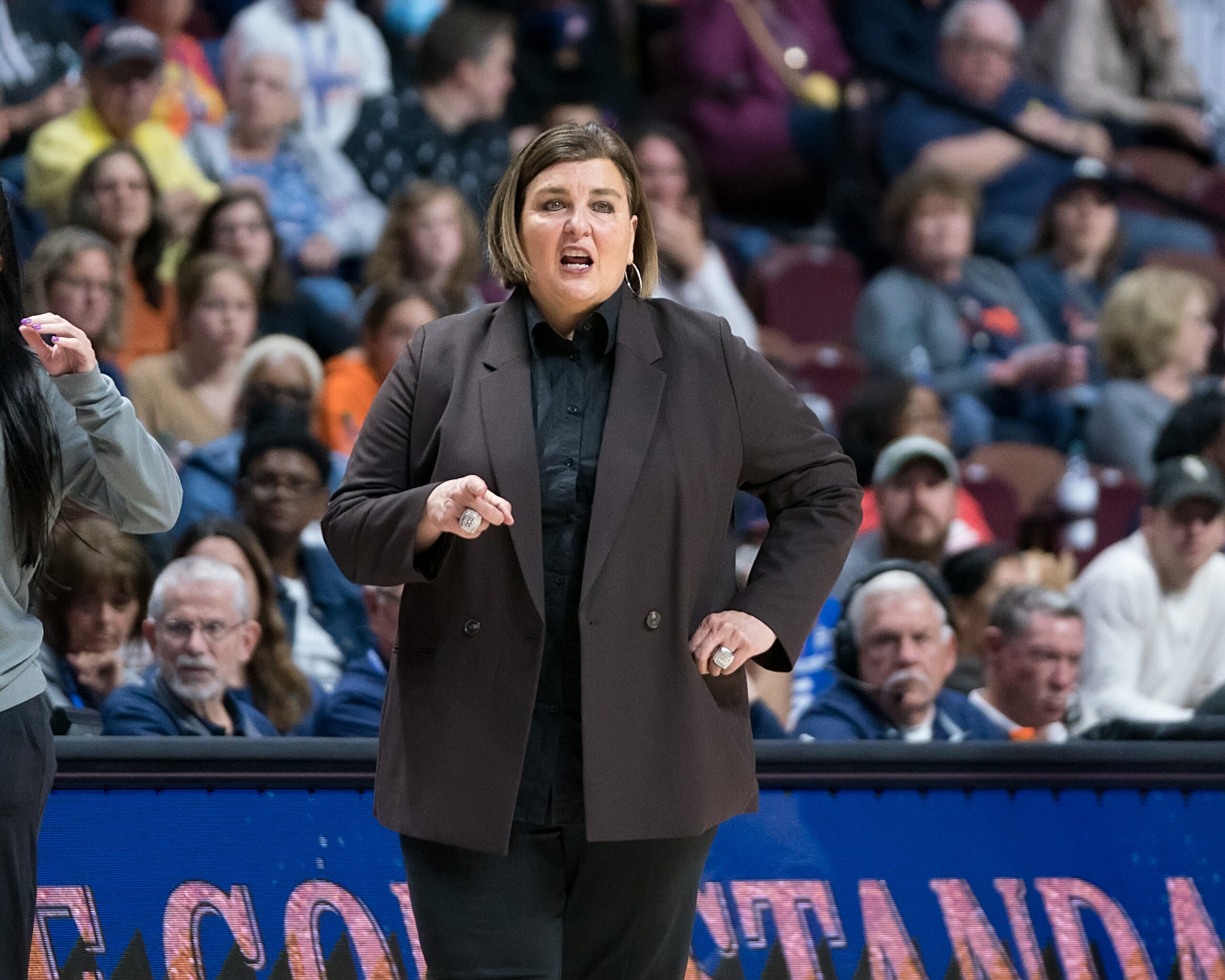 Dallas Wings head coach Latricia Trammell directs her team from the sideline during a regular season game. She's wearing black clothing underneath a dark grey blazer.