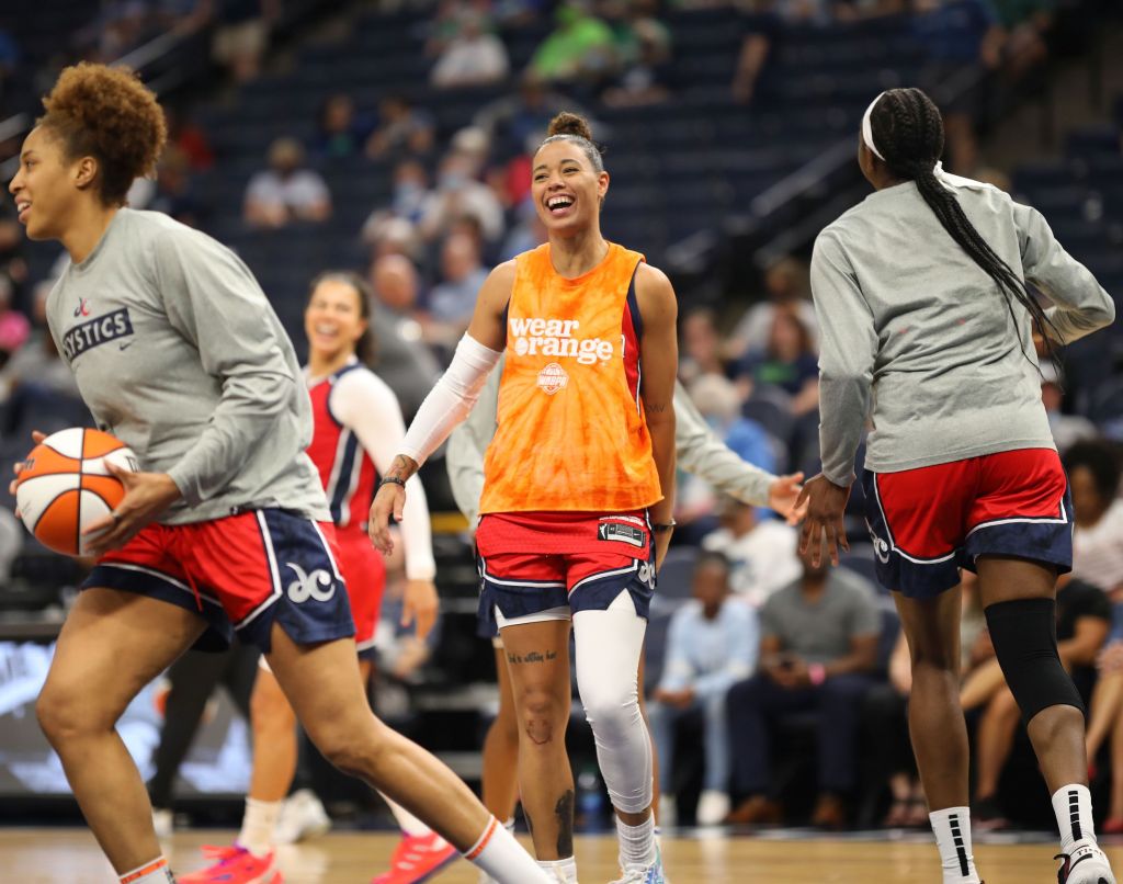 Washington Mystics guard Natasha Cloud smiles during warm-ups. She is wearing an orange shirt with the sleeves cut off that says "Wear Orange" in honor of gun violence victims and survivors.