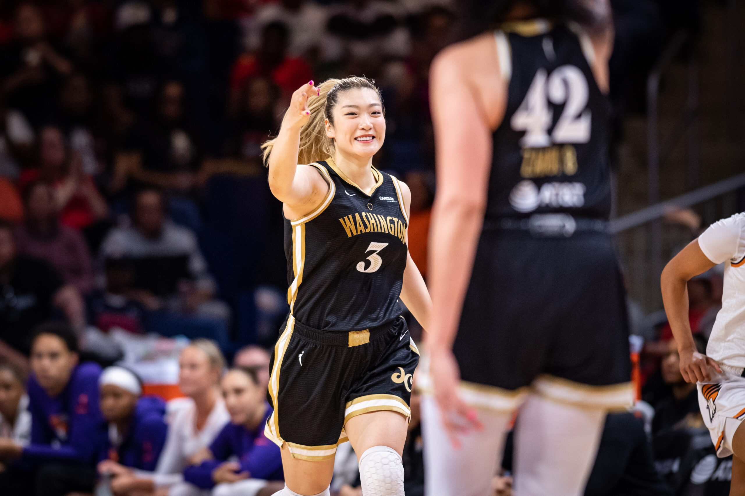 Washington Mystics guard Li Meng grins and makes a 3-point sign with her right hand as she runs back on defense.