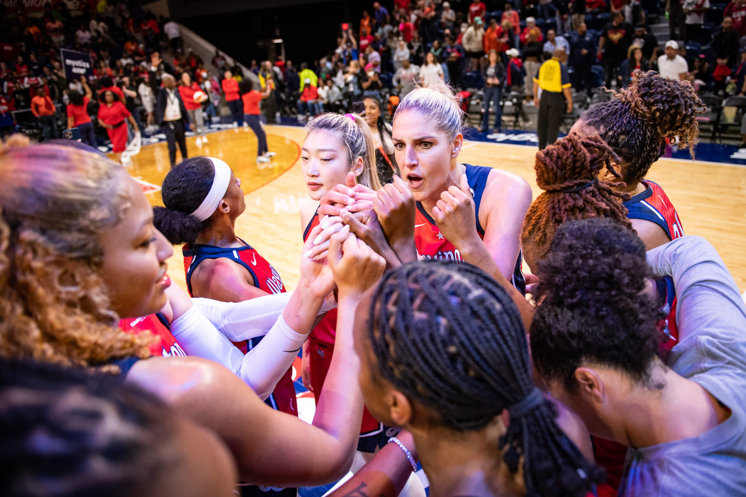 The Washington Mystics huddle after a game, putting their fists into the center. Forward/guard Elena Delle Donne addresses the group.
