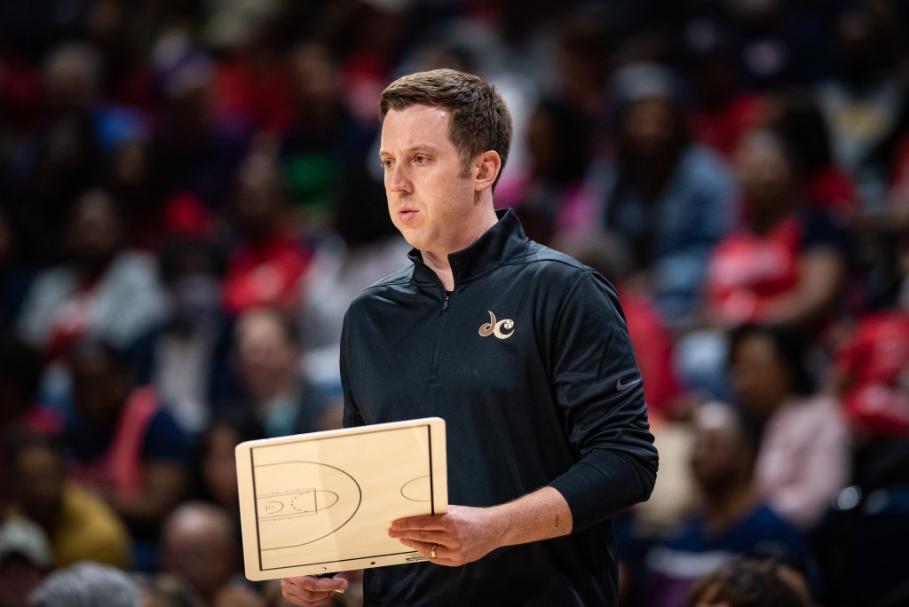 Washington Mystics head coach Eric Thibault stares into the distance with no one around him. He holds a dry erase board in his left hand.
