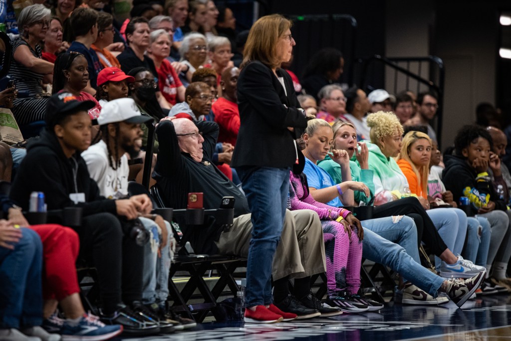Washington Mystics general manager Mike Thibault sits in a courtside seat with his hands on his head, watching his team play. His wife Nanci stands next to him and watches with her arms crossed.