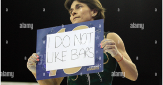 Oksana Chusovitina telling it like it is, holding a sign that says "I DO NOT LIKE BARS". Photo credit: Andrew Orchard Sports Photography.