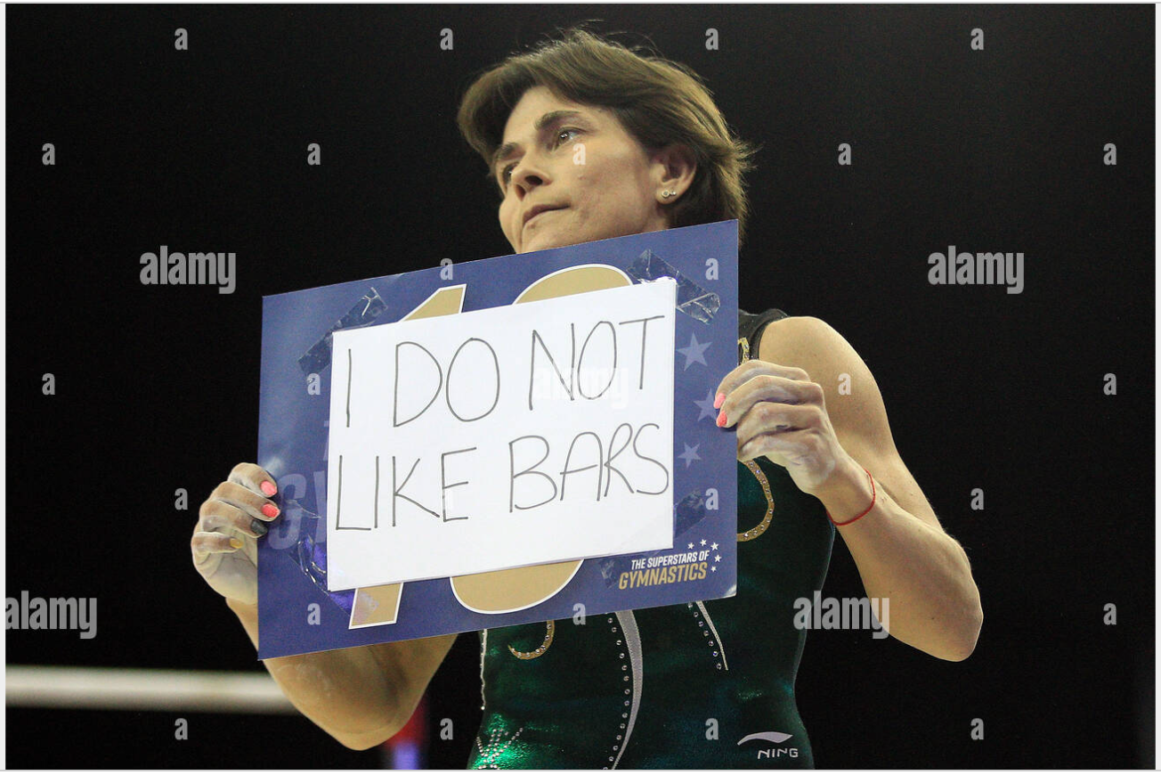 Oksana Chusovitina telling it like it is, holding a sign that says "I DO NOT LIKE BARS". Photo credit: Andrew Orchard Sports Photography.