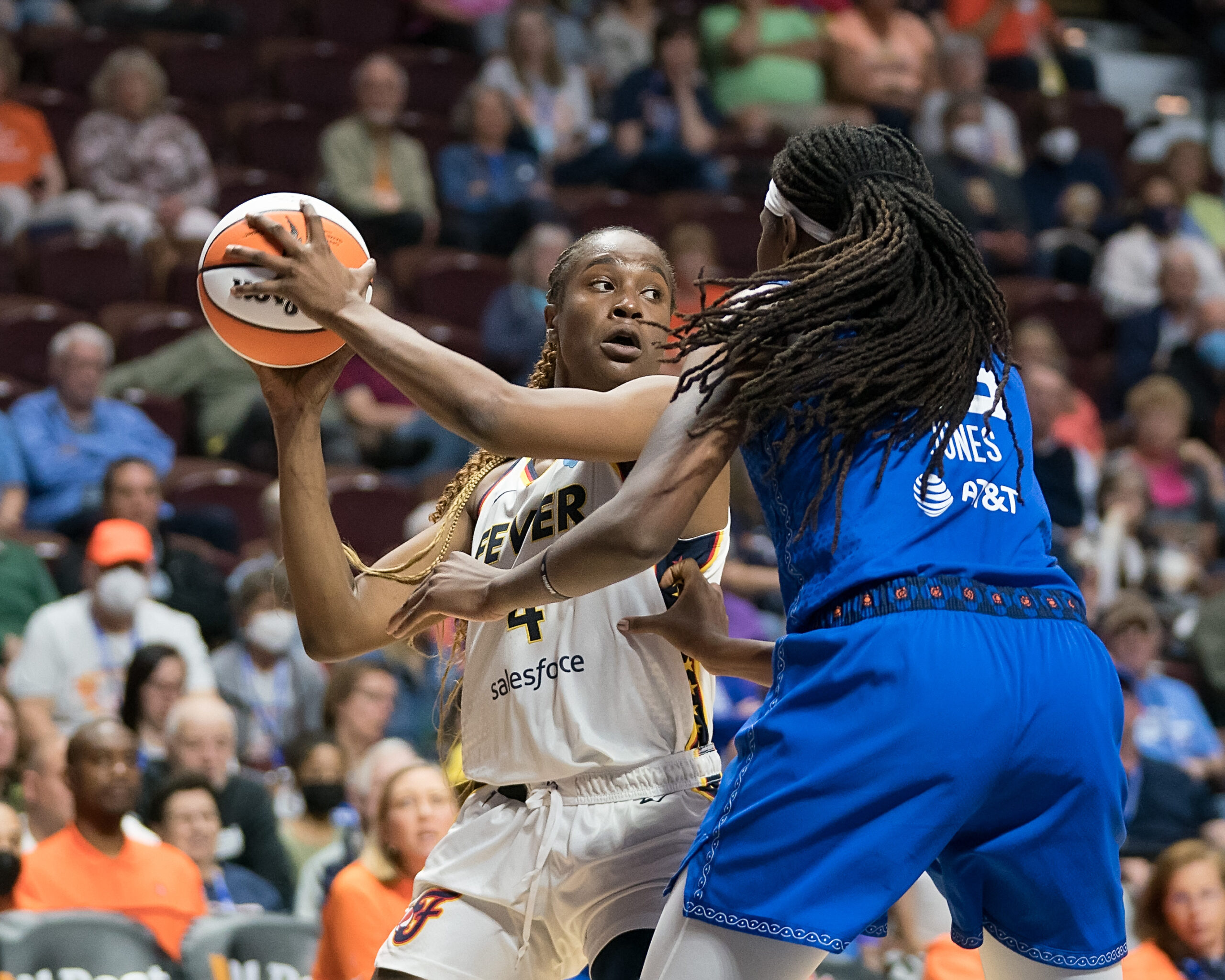 Indiana Fever center Queen Egbo holds the ball with two hands on the right side of her head, scanning the court as a Connecticut Sun player defends.