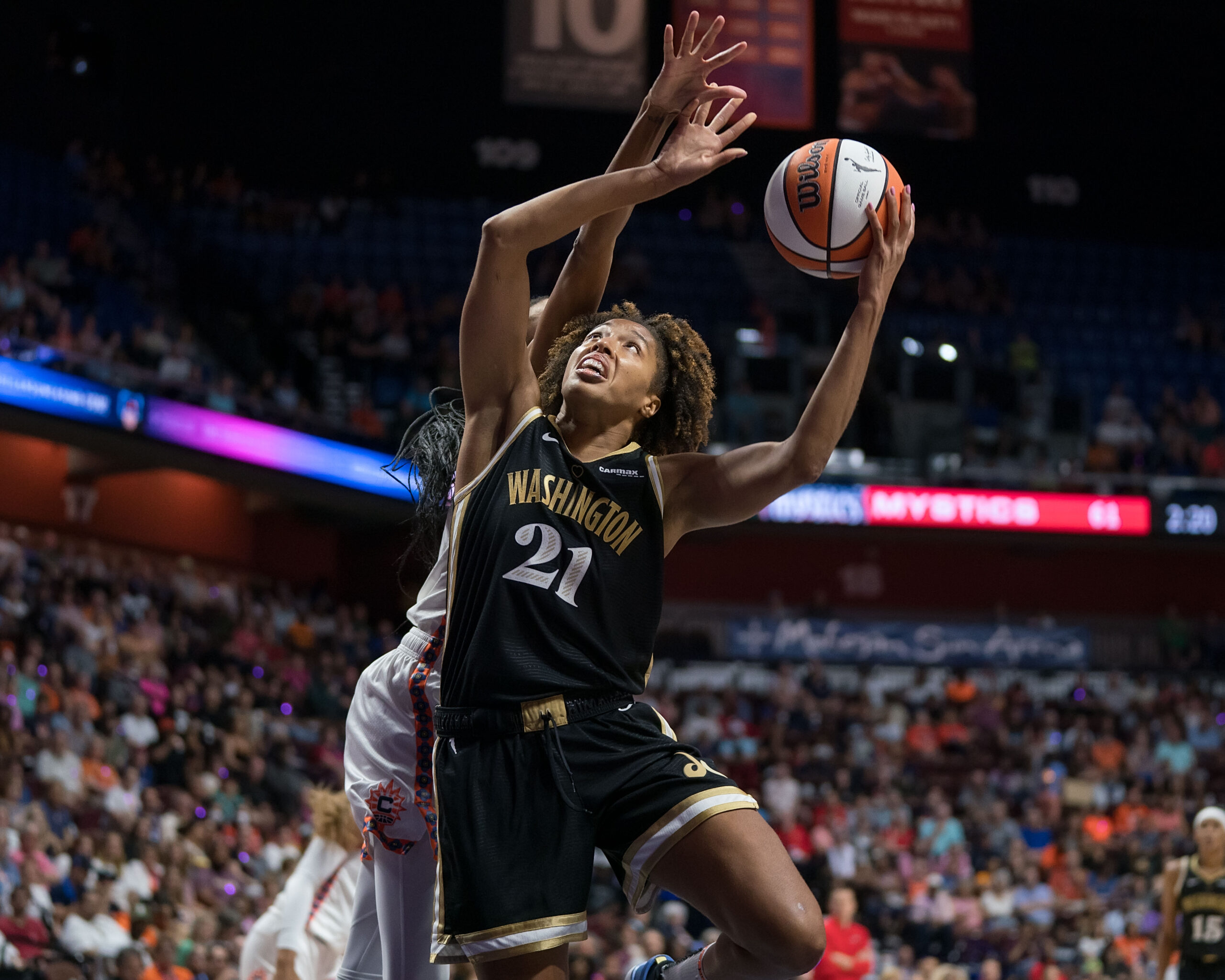 Washington Mystics forward Tianna Hawkins shoots the ball with her left hand while absorbing contact from behind from Connecticut Sun forward/guard DeWanna Bonner.